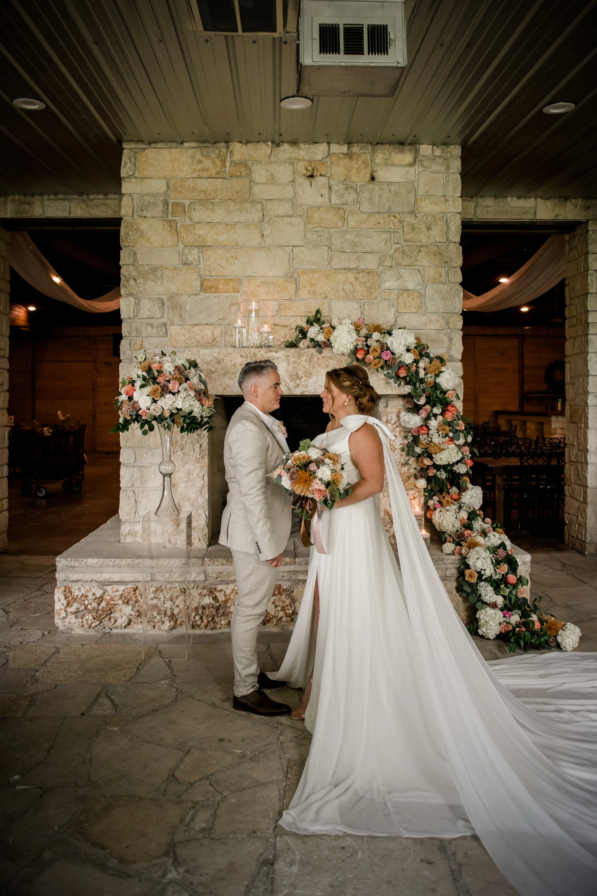 A bride and groom exchanging vows in front of a stone fireplace decorated with floral arrangements at their wedding ceremony.