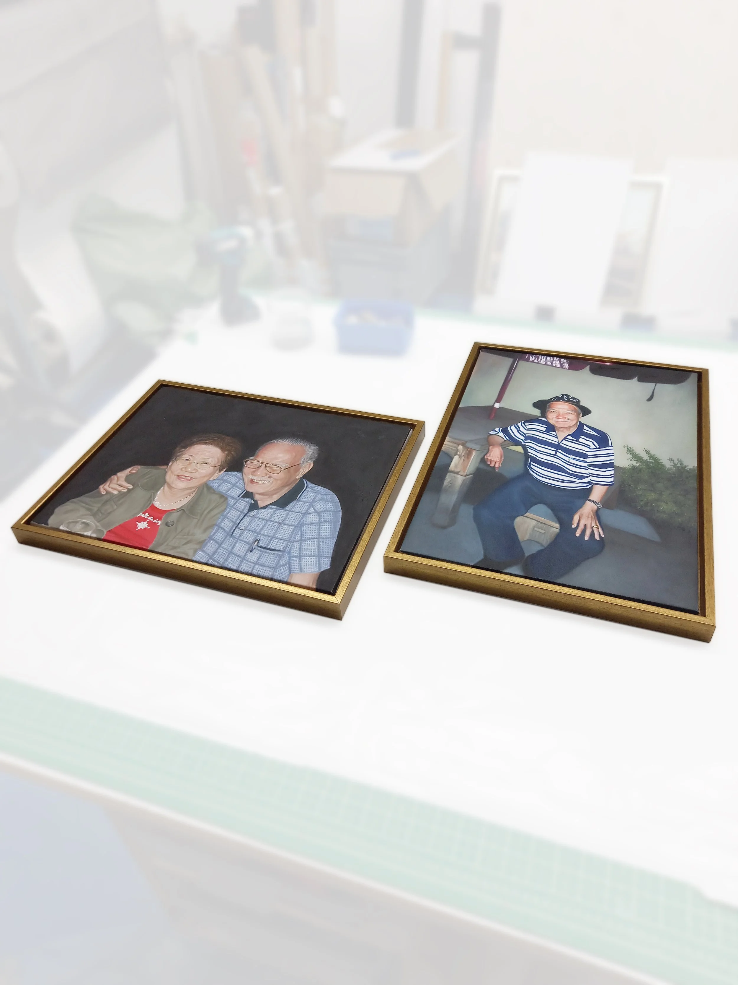 Two framed photographs of elderly people, one with a woman and man smiling and the other with a woman sitting outdoors, placed on a light-colored surface.