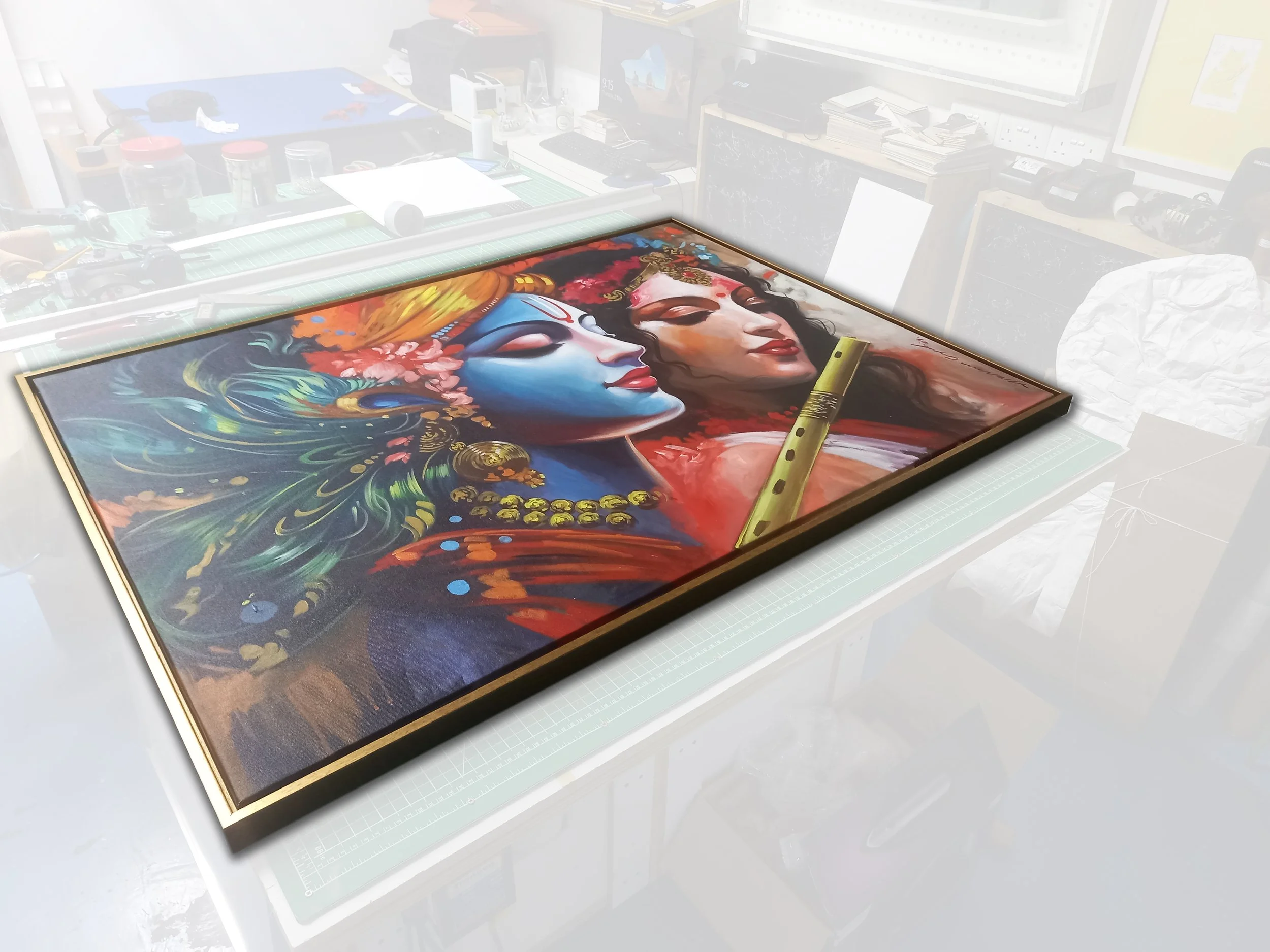 A colorful painting of goddess-like figures with intricate jewelry and floral adornments, lying on their sides with eyes closed, resting on a table in an artist's workspace.