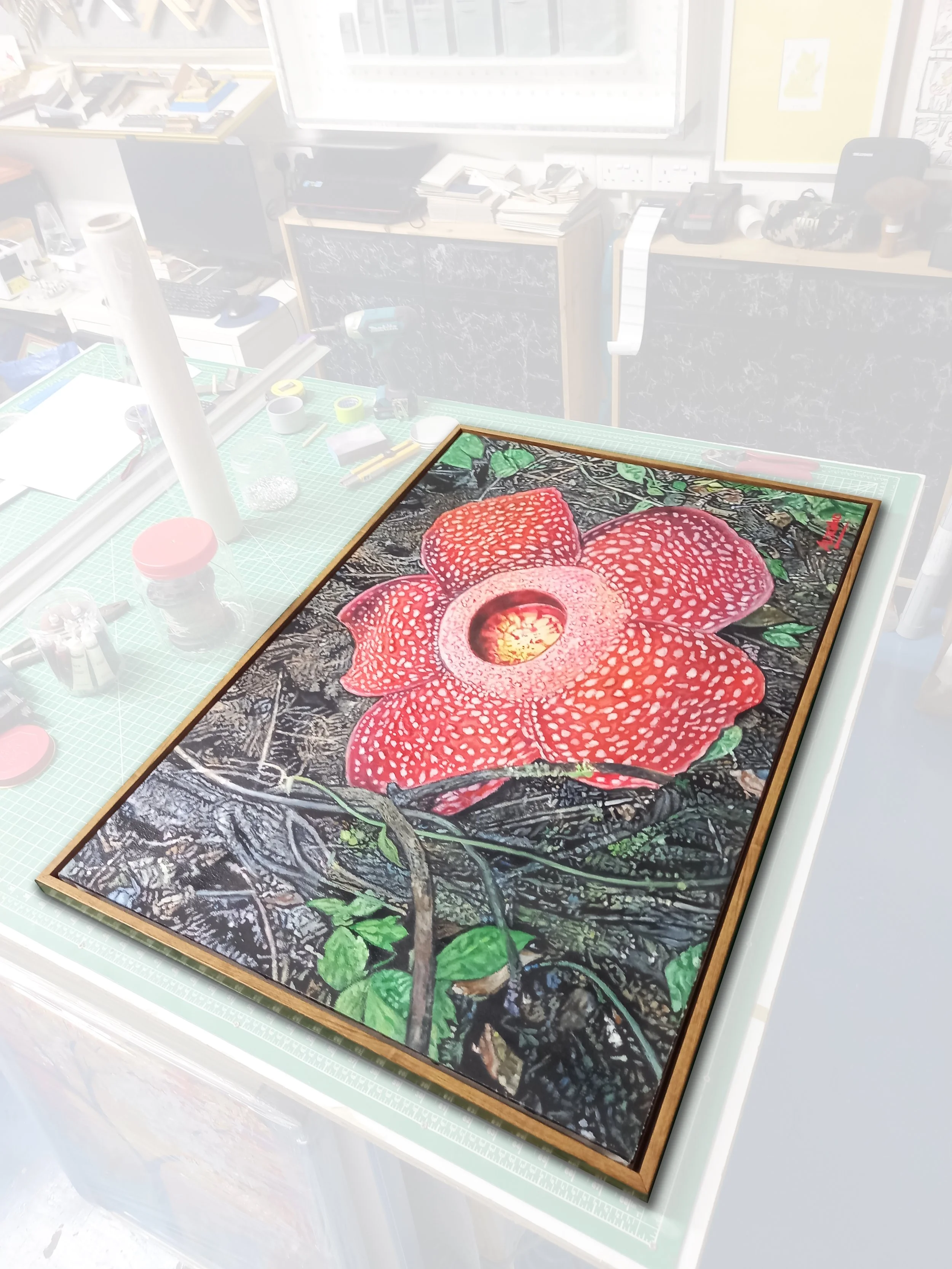 A framed artwork depicting a large red flower with white and red speckled petals and green leaves, set against a dark, textured background with tree branches.
