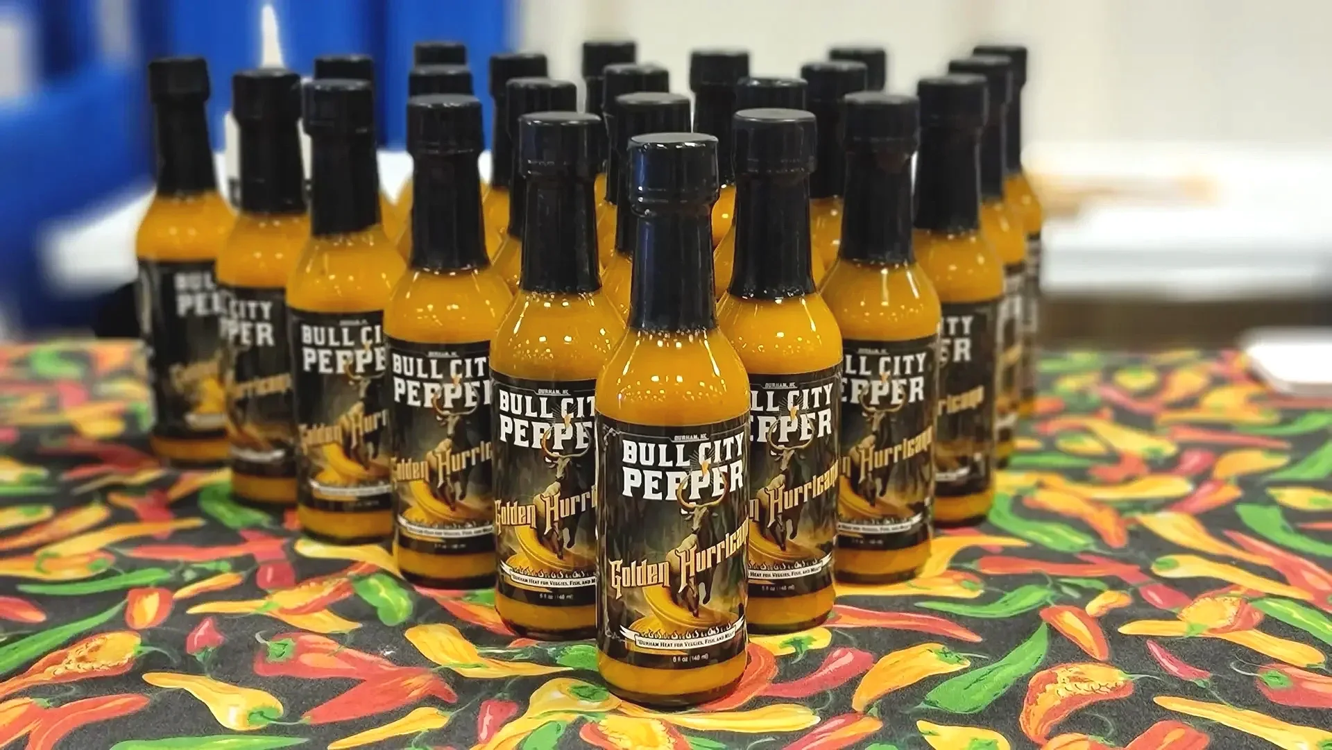 A group of hot sauce bottles labeled 'Bull City Pepper' with 'Golden Hurricane' flavor on a colorful tablecloth.
