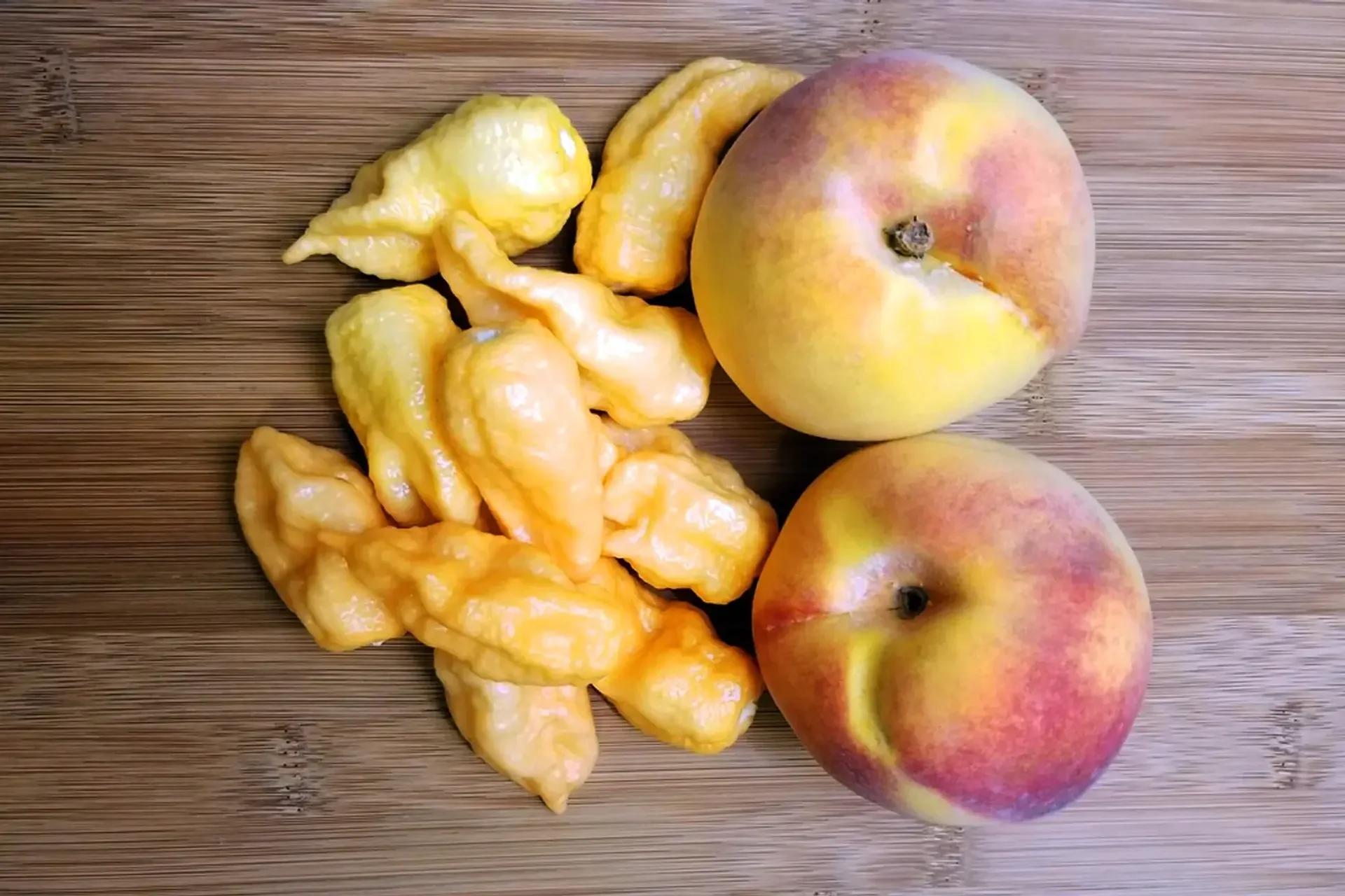 Two peaches and peach ghost chili peppers on a wooden surface.
