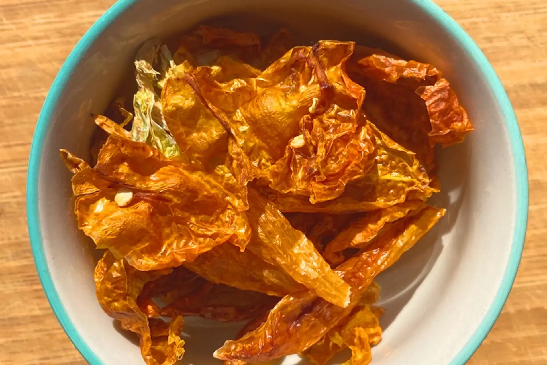 Dried orange peels in a round ceramic bowl on a wooden surface.