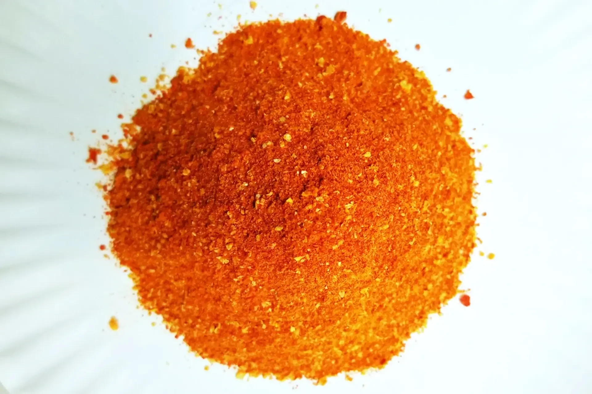 Close-up of a pile of red chili powder on a white surface.