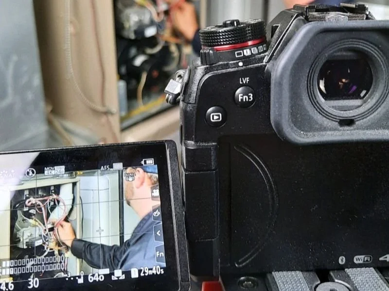 A digital camera capturing a technician working on an electrical panel with wiring.