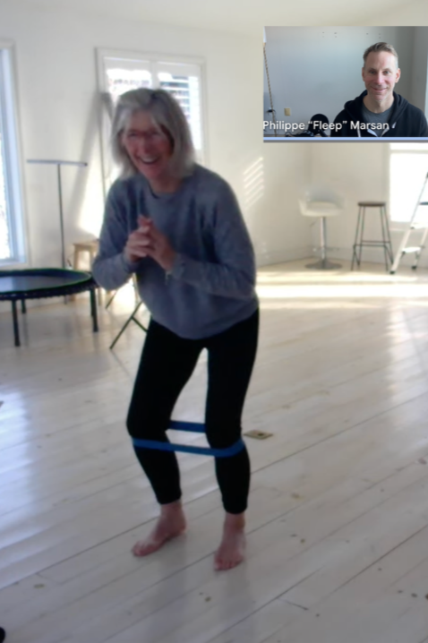 Lady smiling as she performs an exercise with a resistance band around her knees and Philippe watches live on video