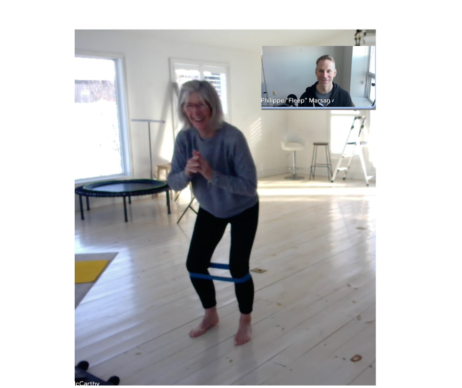 Lady smiling as she performs an exercise with a resistance band around her knees and Philippe watches live on video