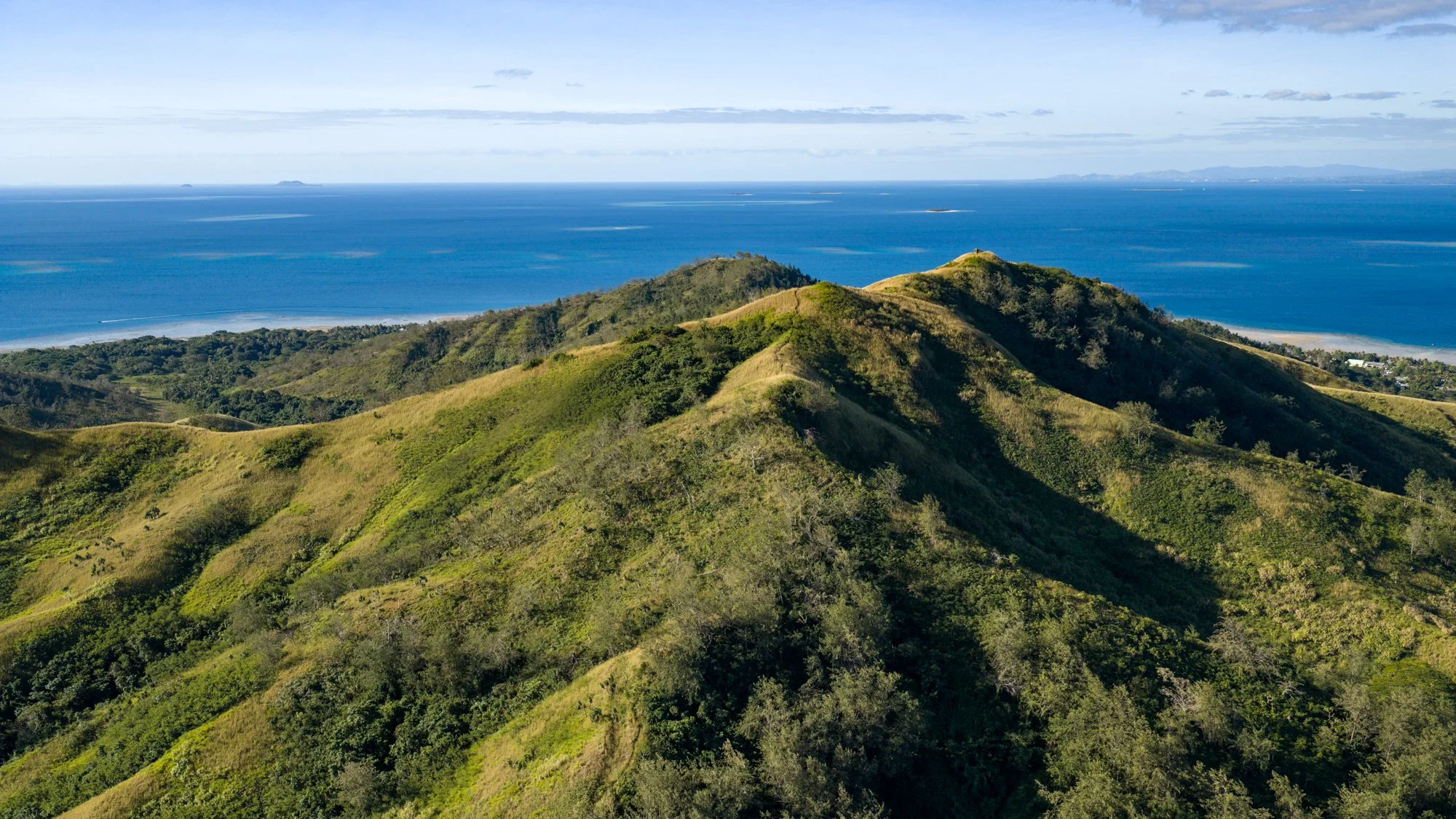 Aerial view of lush green ridges rising above the blue South Pacific in Fiji.