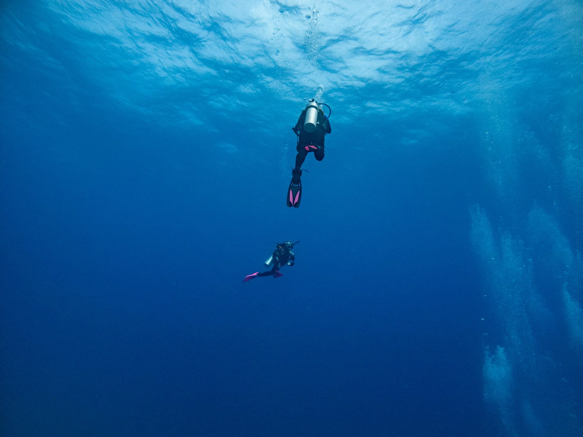 Scuba divers descending through deep blue Caribbean water near Jamaica.