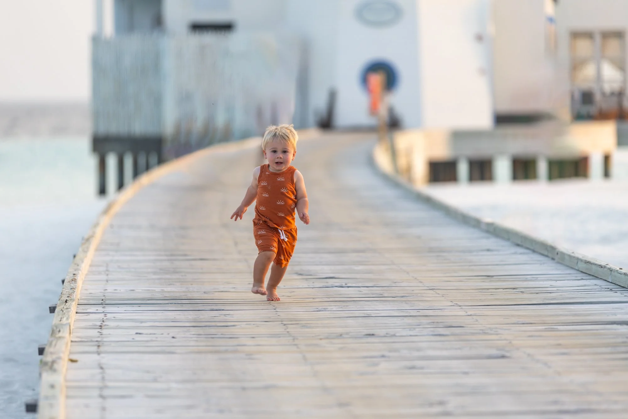 Young child running along a boardwalk toward a blue-and-white lighthouse in the Maldives.