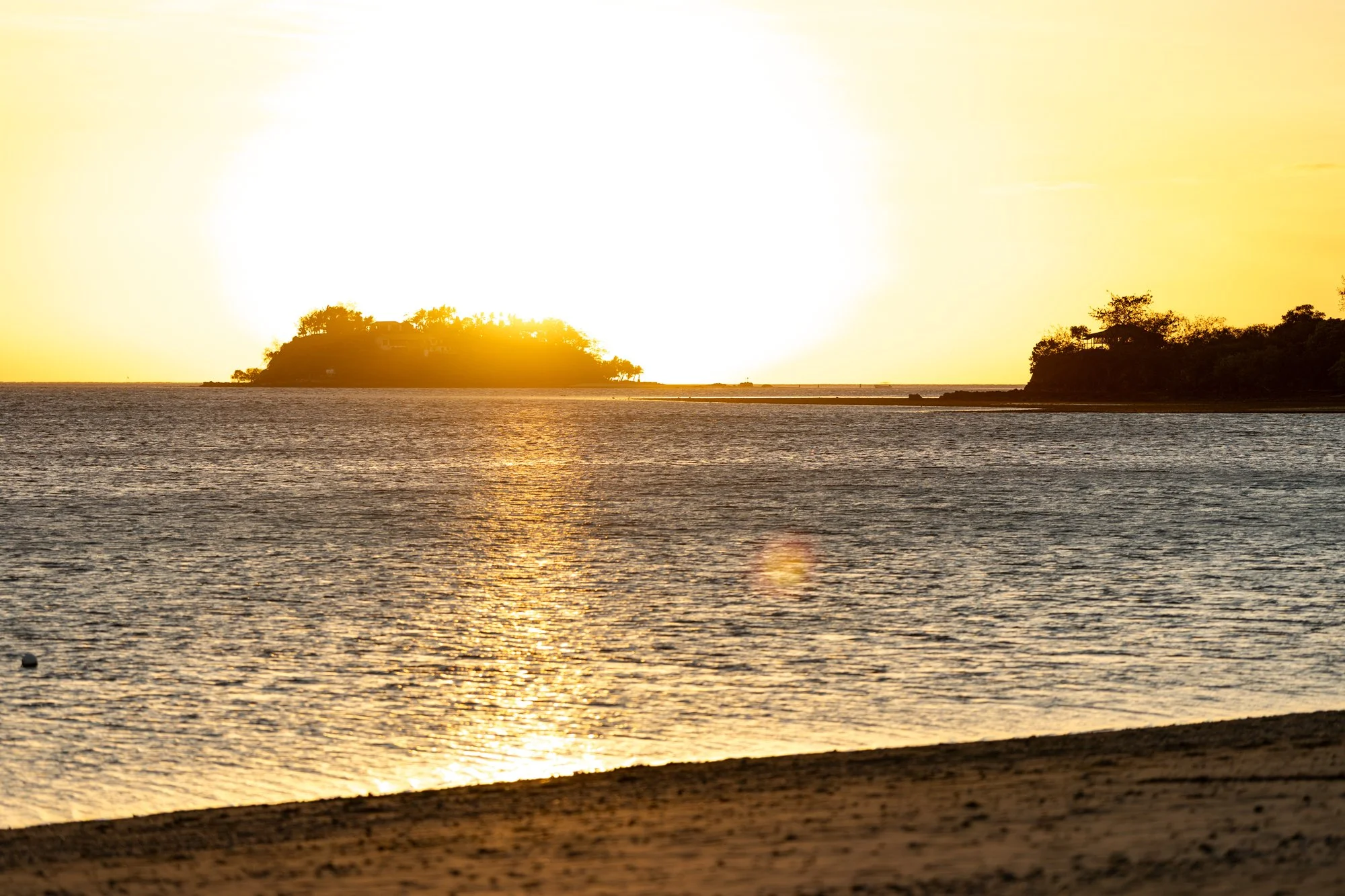 The setting sun glows between two Fijian islands and reflects across the calm sea.