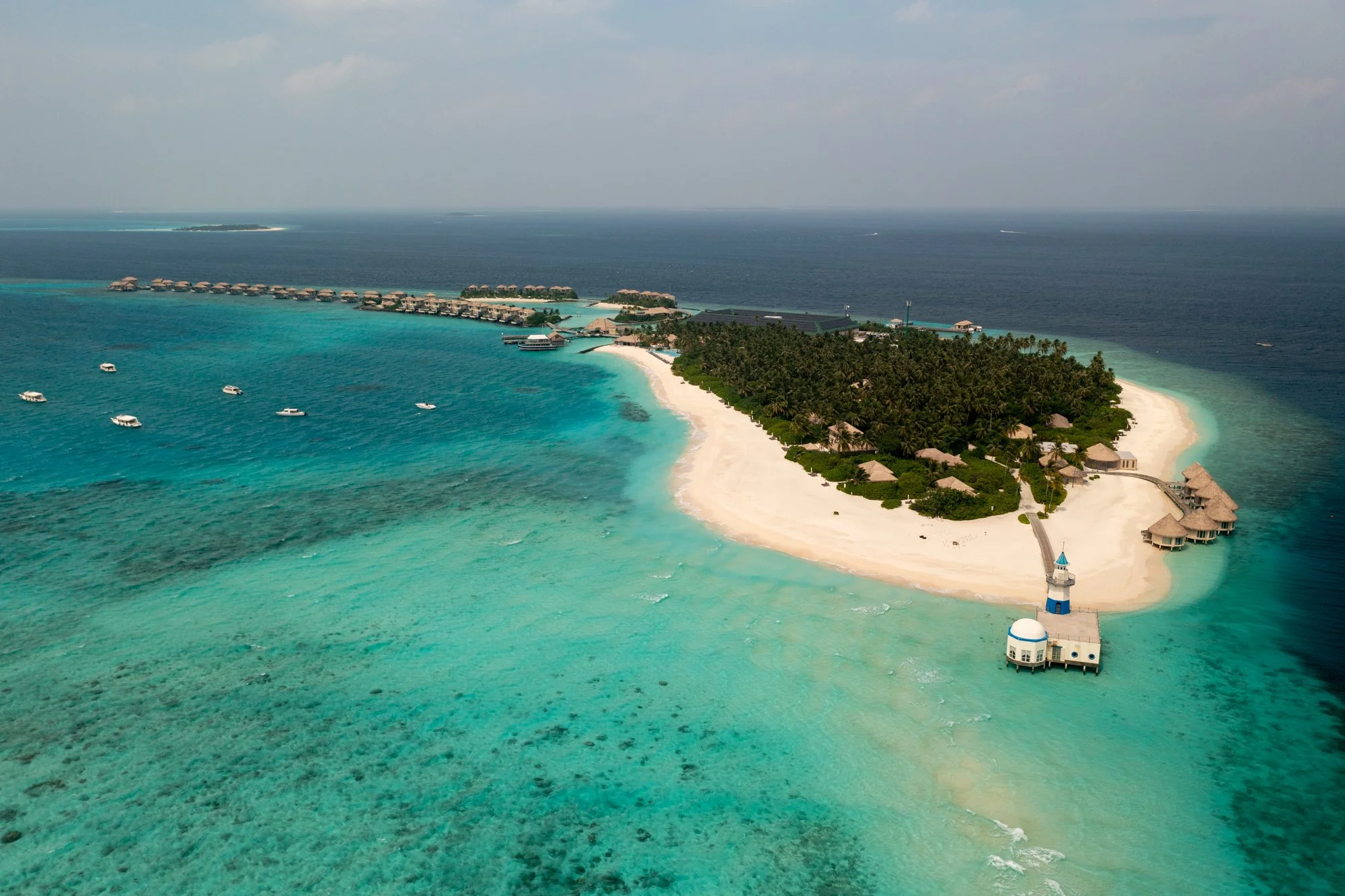 Small tropical island surrounded by pale sandbars and turquoise water in the Maldives.