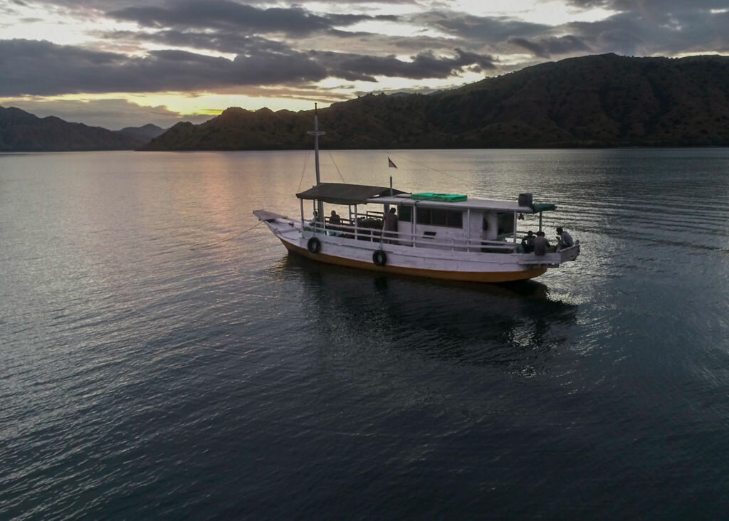 Traditional boat crossing calm water at sunset in Komodo National Park