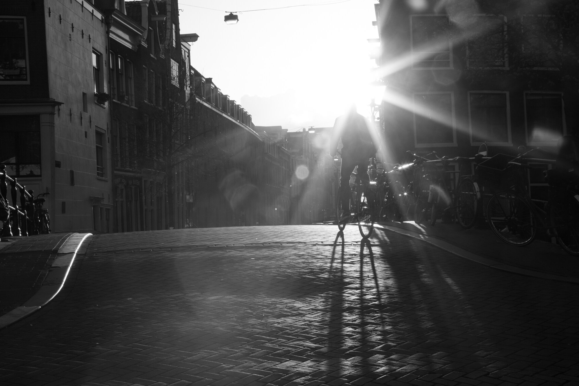 Black-and-white street scene with a cyclist and bicycles at sunset in Amsterdam