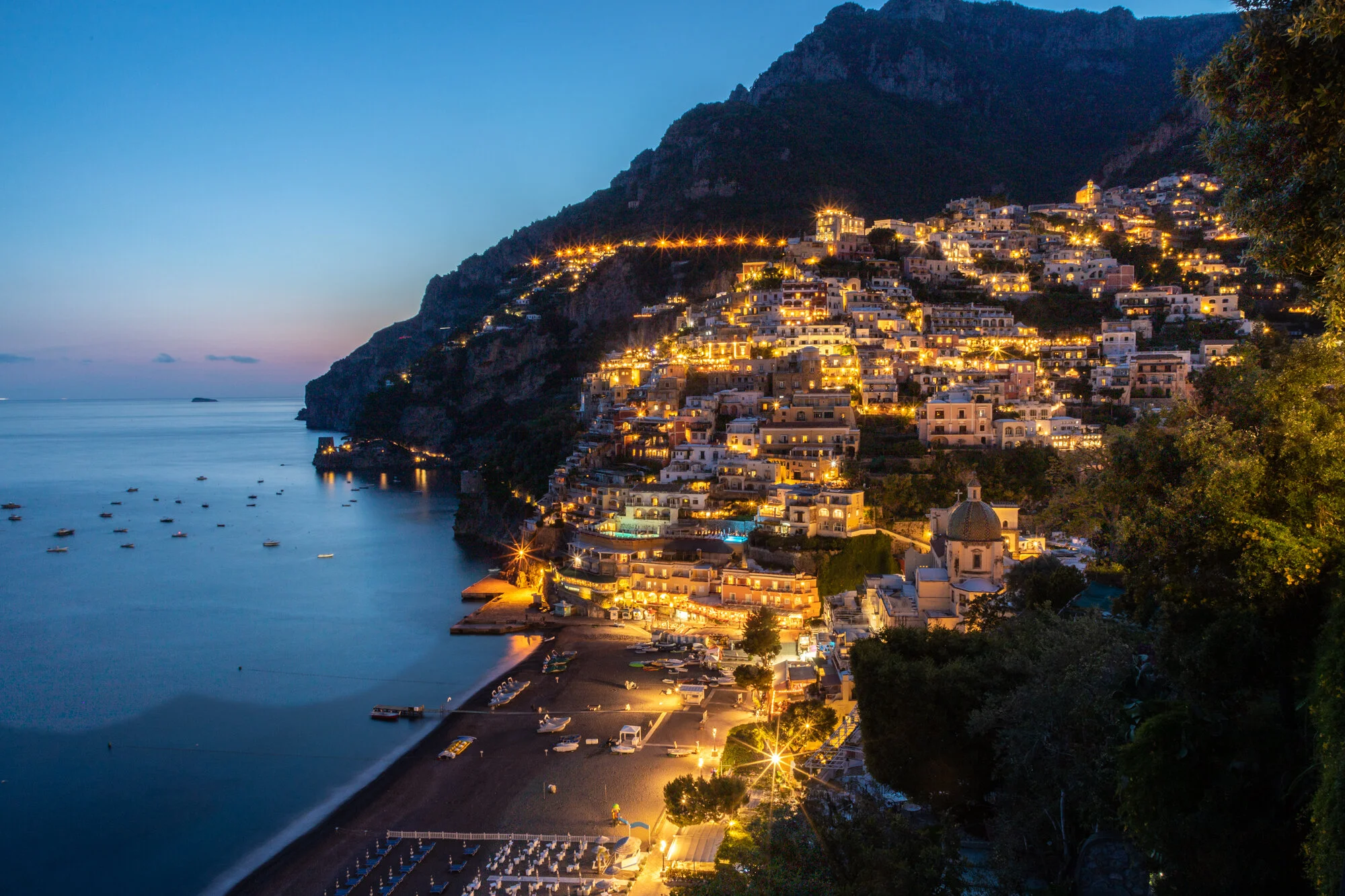Positano's illuminated hillside and coastline at blue hour on the Amalfi Coast, Italy.