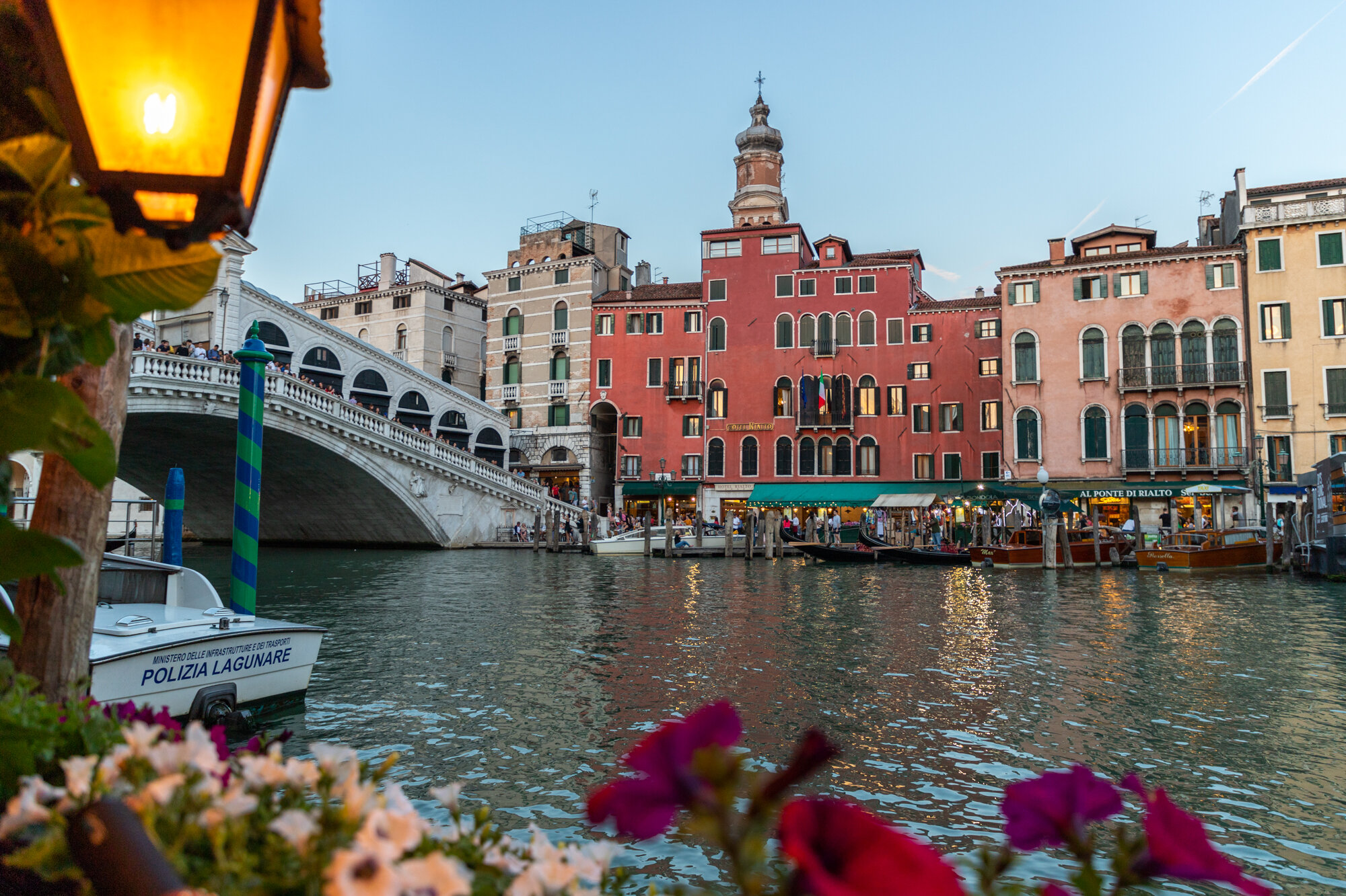 Grand Canal and Rialto Bridge in Venice framed by a glowing lantern and flowers.