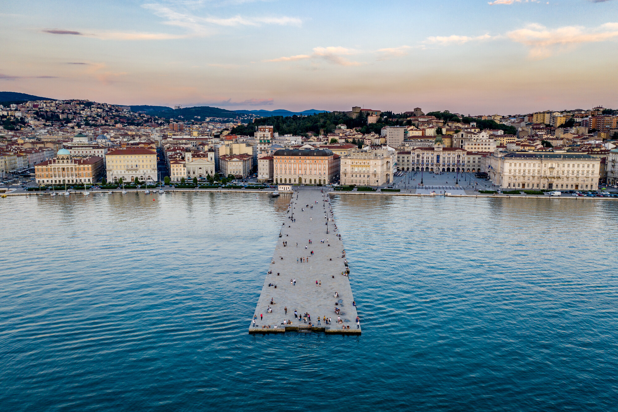 Aerial view along Molo Audace toward the Trieste waterfront at sunset.