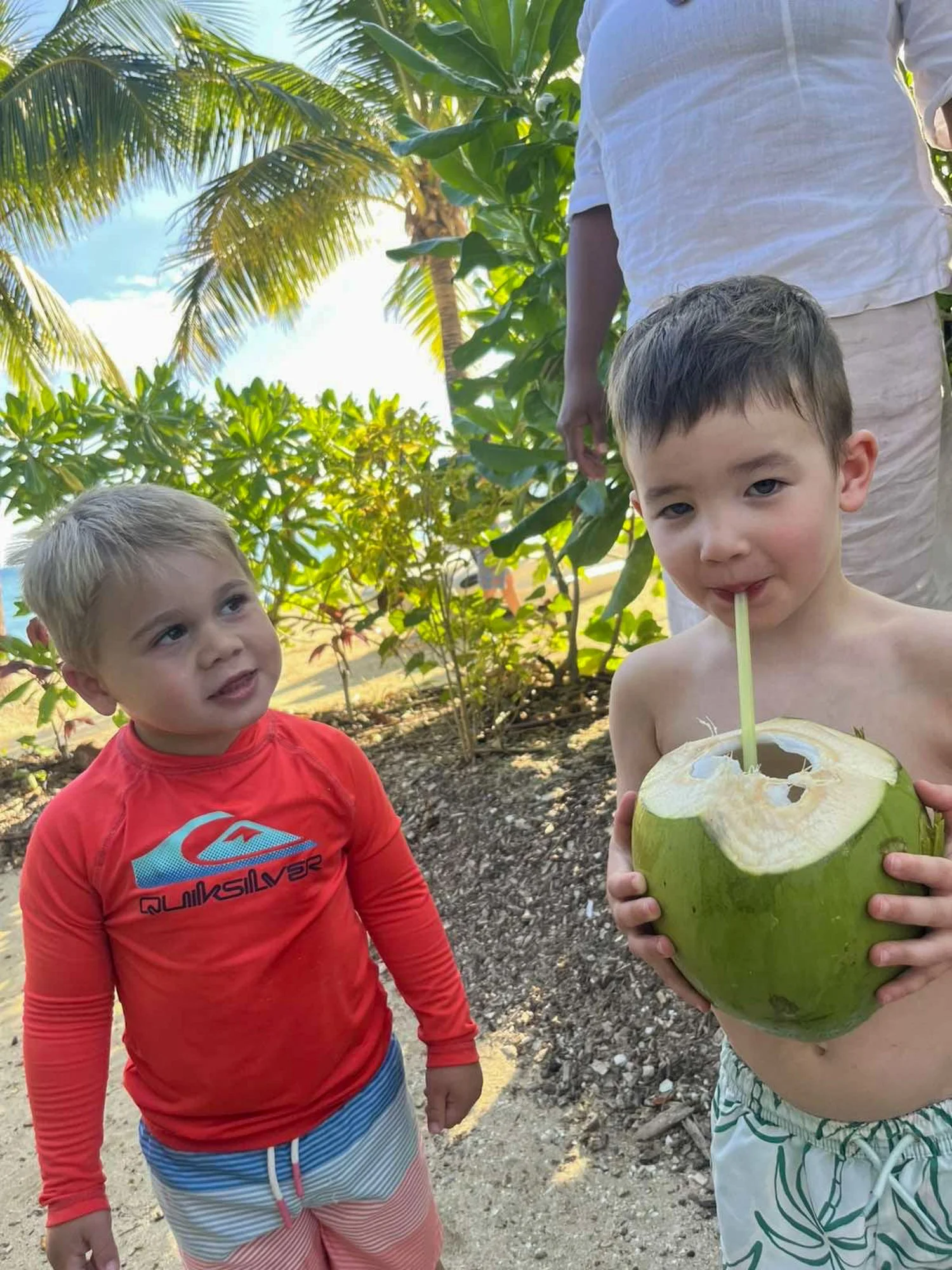 Two young children share a fresh green coconut beneath tropical palms in Fiji.