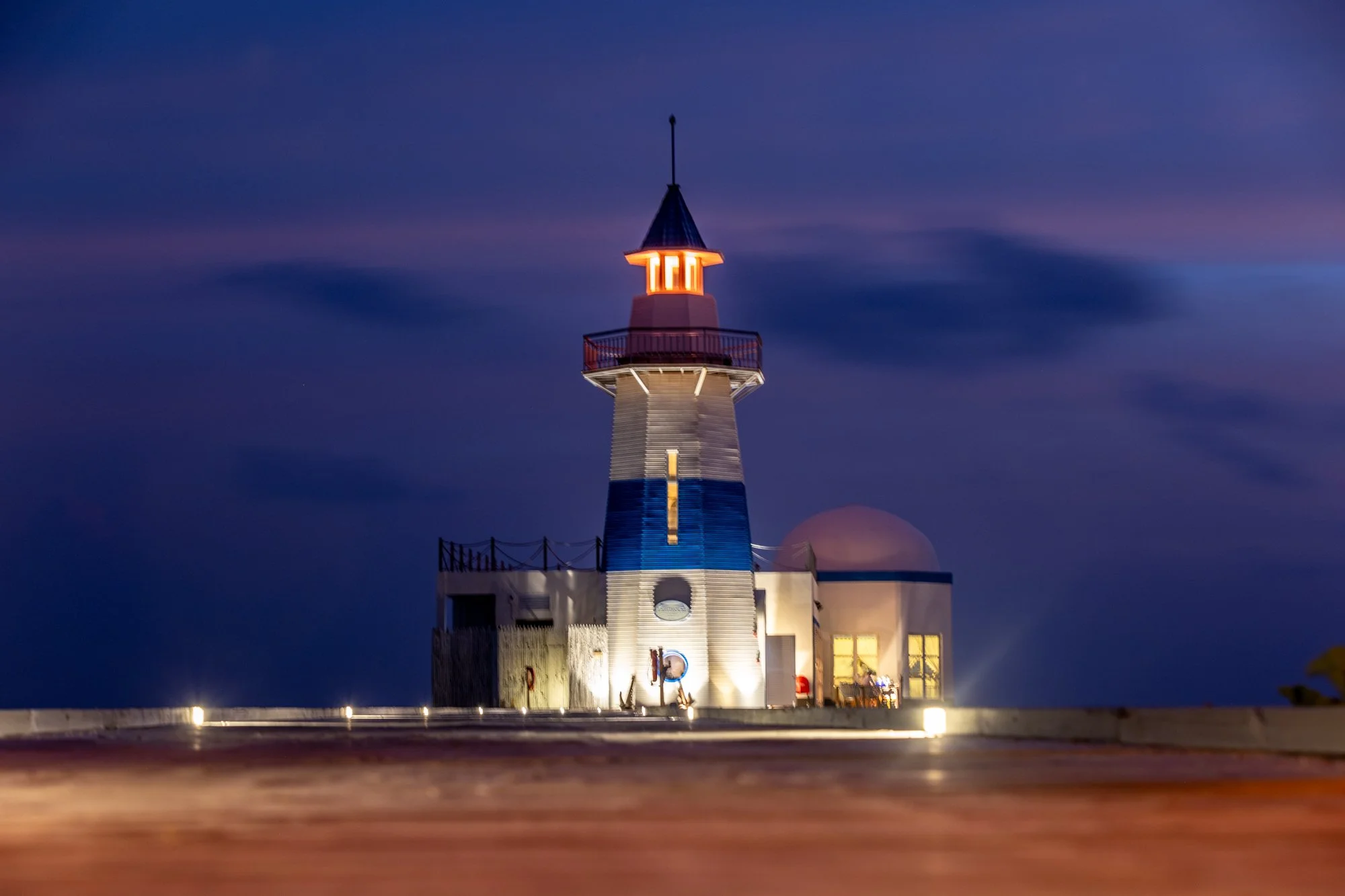 Blue-and-white lighthouse illuminated after sunset on a Maldives island.