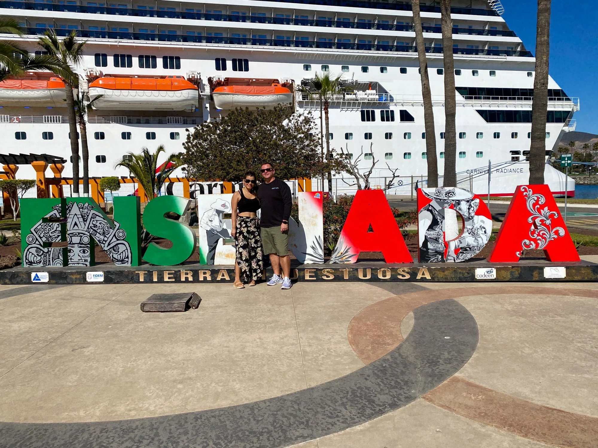 Jason and Amanda at the Ensenada sign with Carnival Radiance docked behind them
