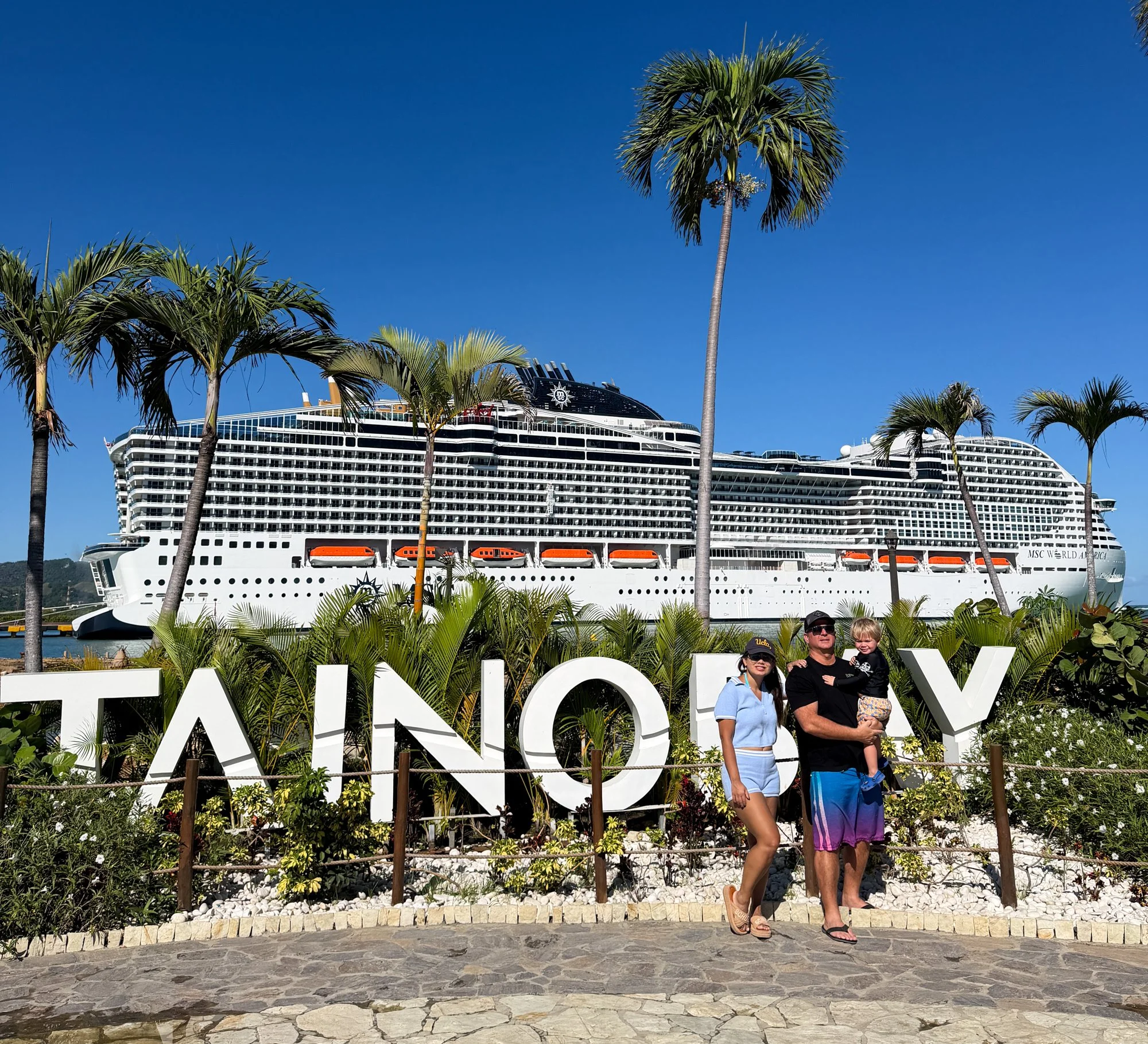 Family posing at Taino Bay with MSC World America docked behind them.