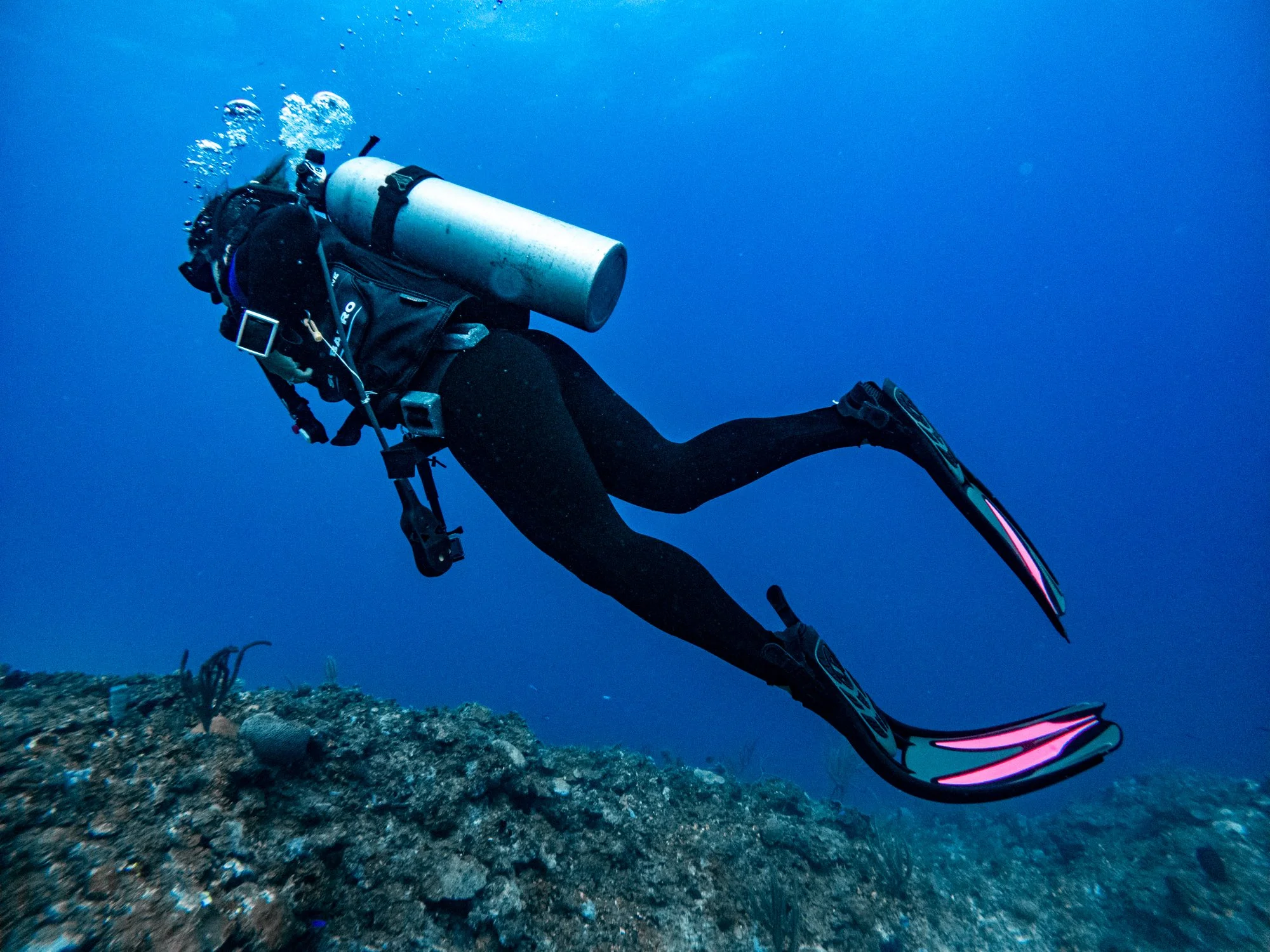 Scuba diver swimming above a coral reef in clear blue water off Jamaica.