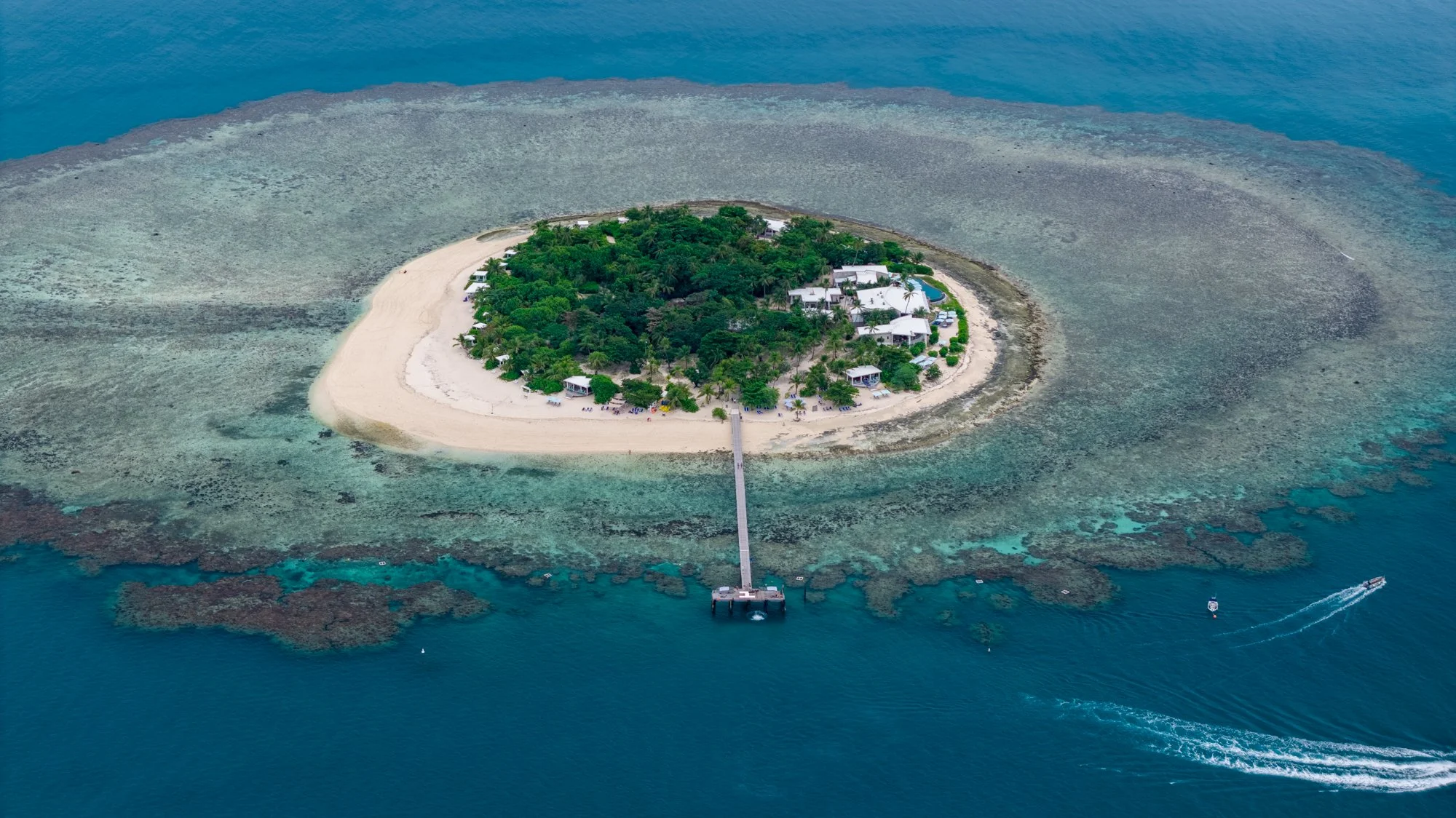 Aerial view of a small Fijian island resort surrounded by coral reef and deep blue water.