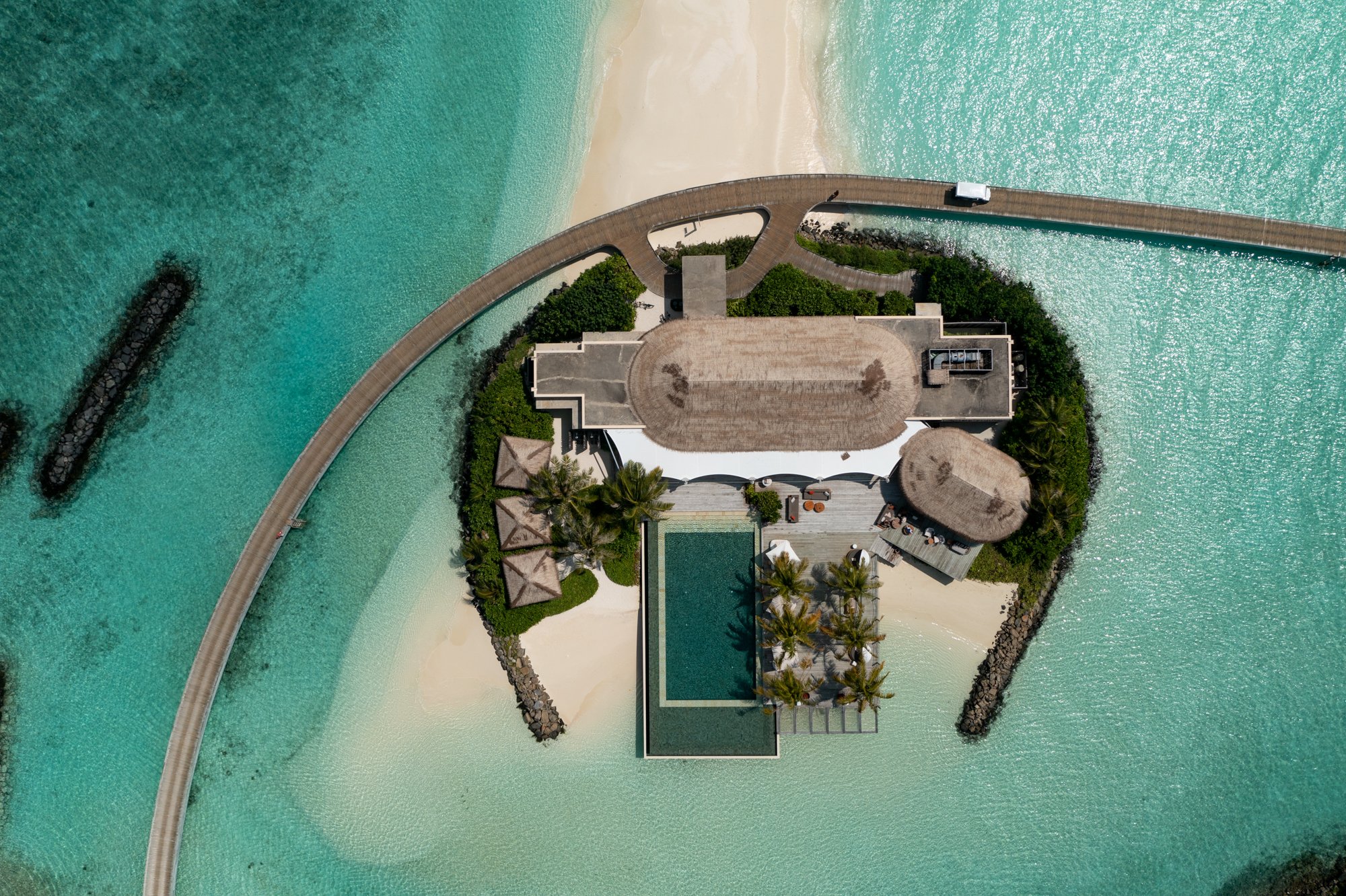 Top-down aerial view of a private island villa, pool, and curved walkway in the Maldives.