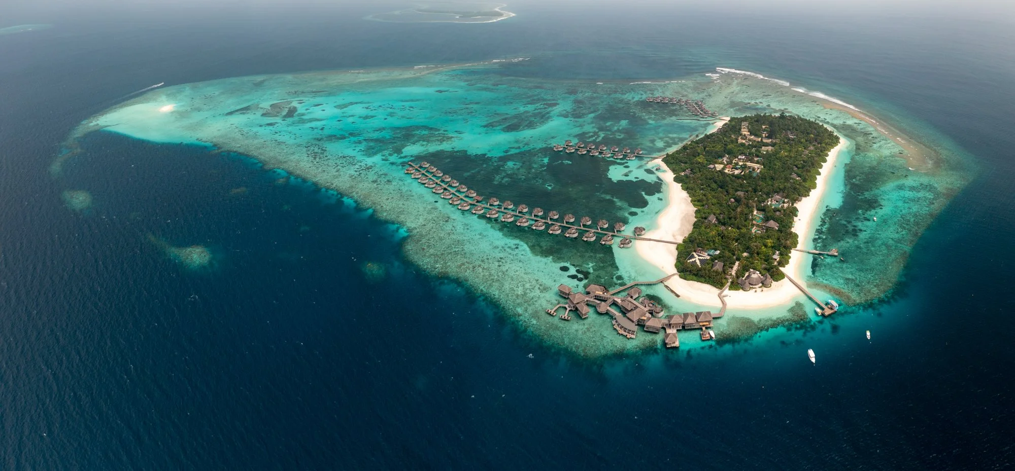 Aerial view of a Maldives island resort surrounded by turquoise reef and overwater villas.