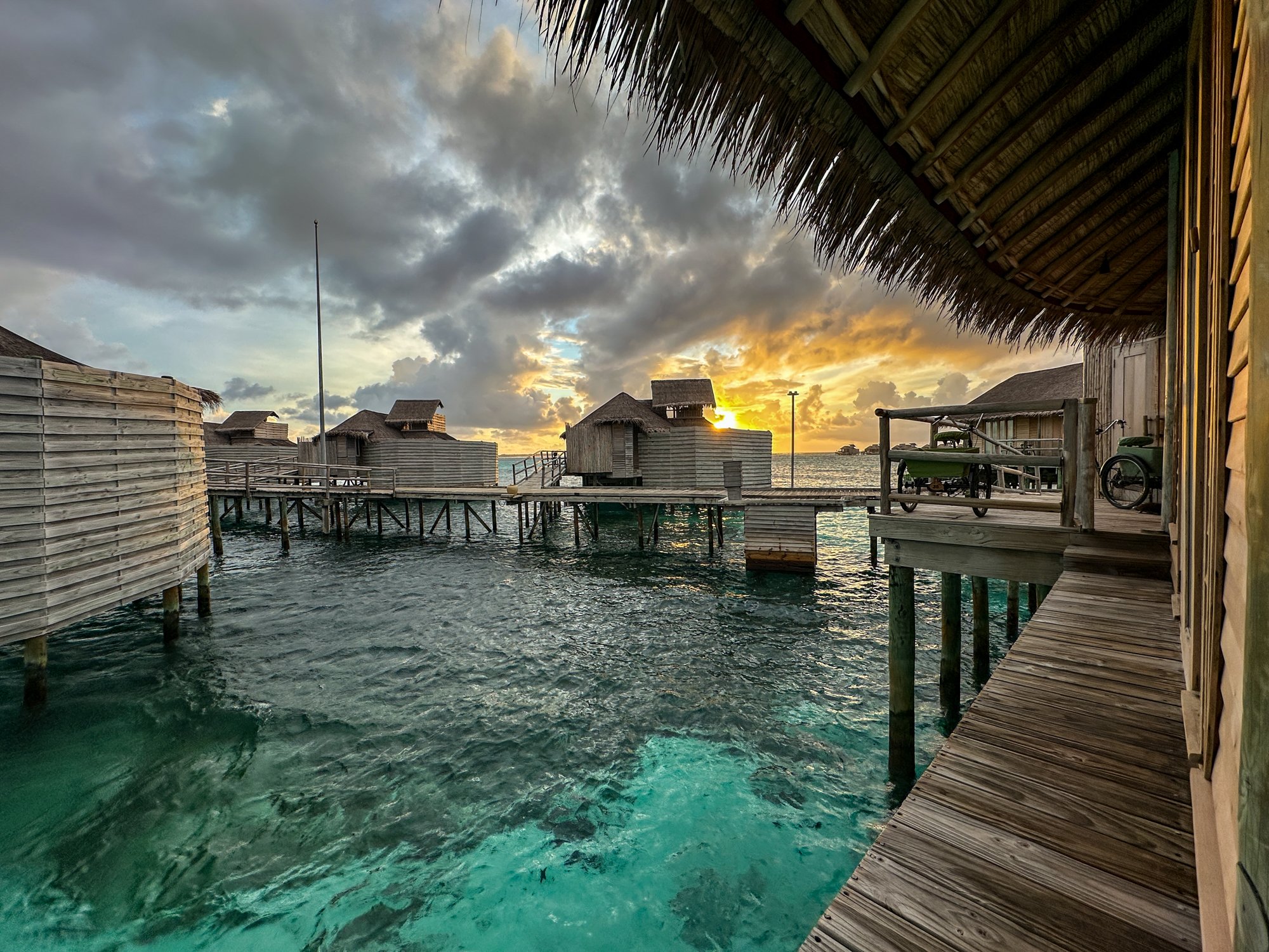 Dramatic tropical sunset breaking through storm clouds above Maldives overwater villas.