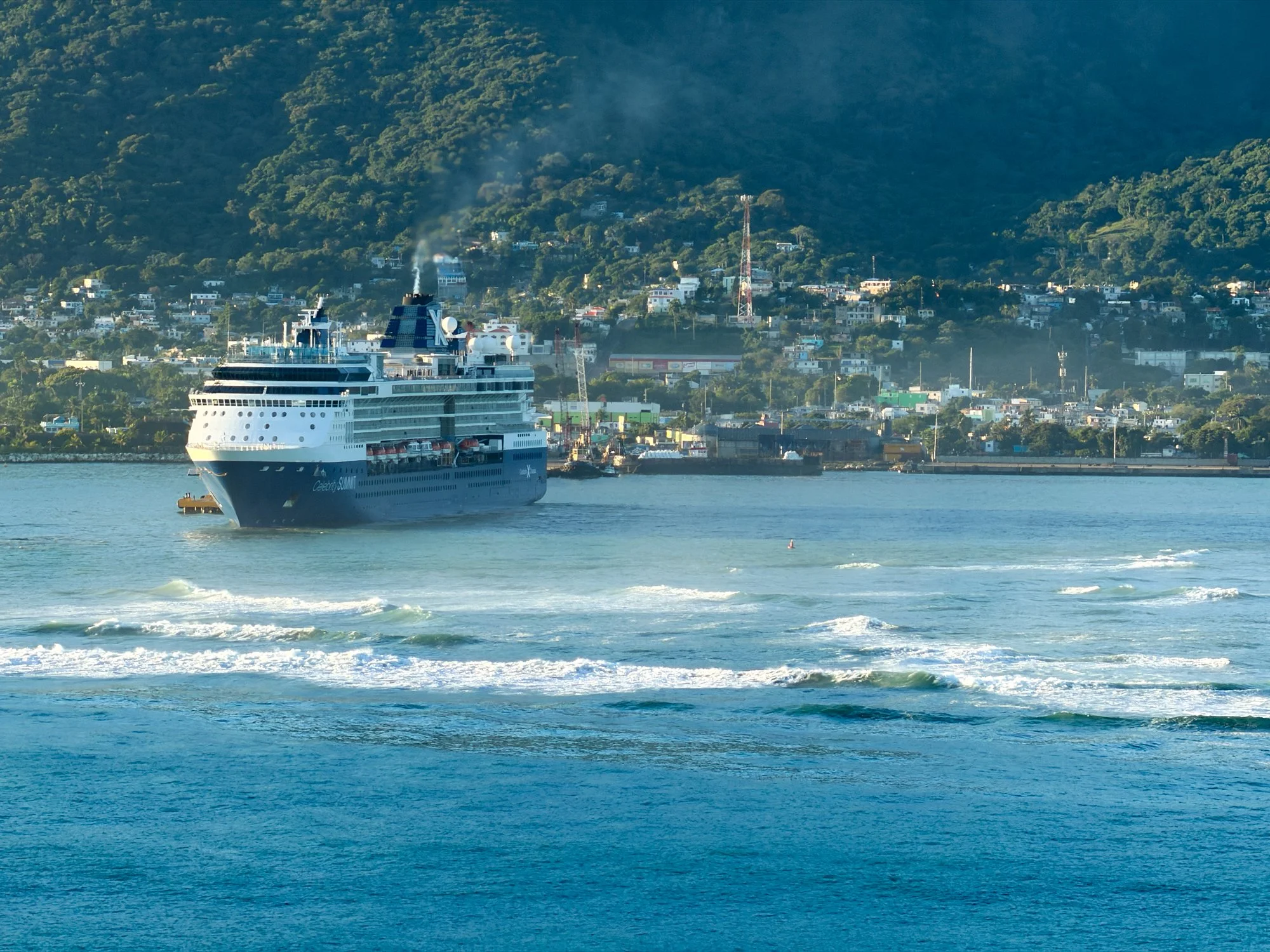 Celebrity Summit sailing from Puerto Plata with the coastal city and mountains behind it.