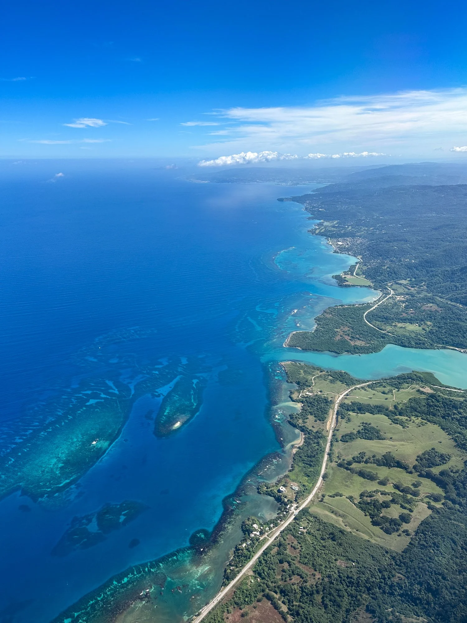 Aerial view of Jamaica’s lush coastline, turquoise lagoons, and offshore coral reefs.