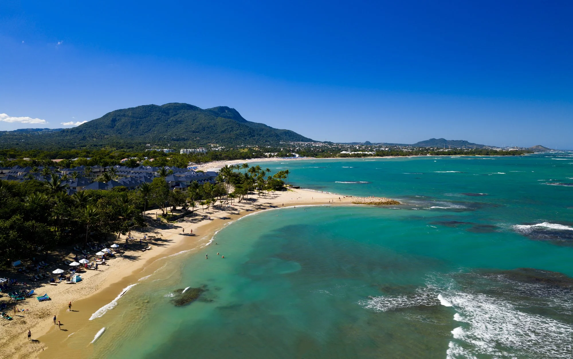 Panoramic aerial view of a palm-lined bay, turquoise water, and mountains near Puerto Plata.