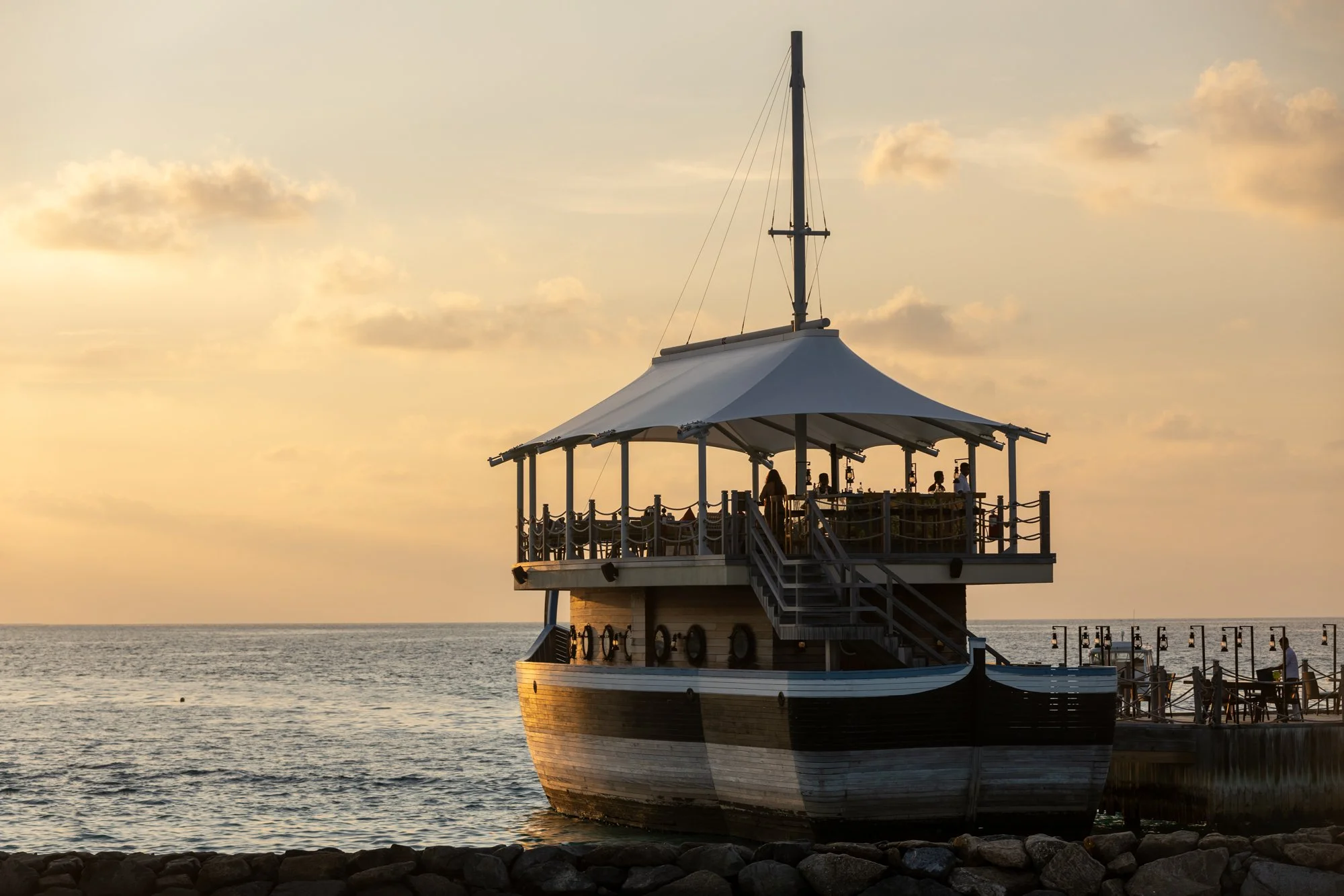 Traditional wooden boat silhouetted against a golden Maldives sunset.