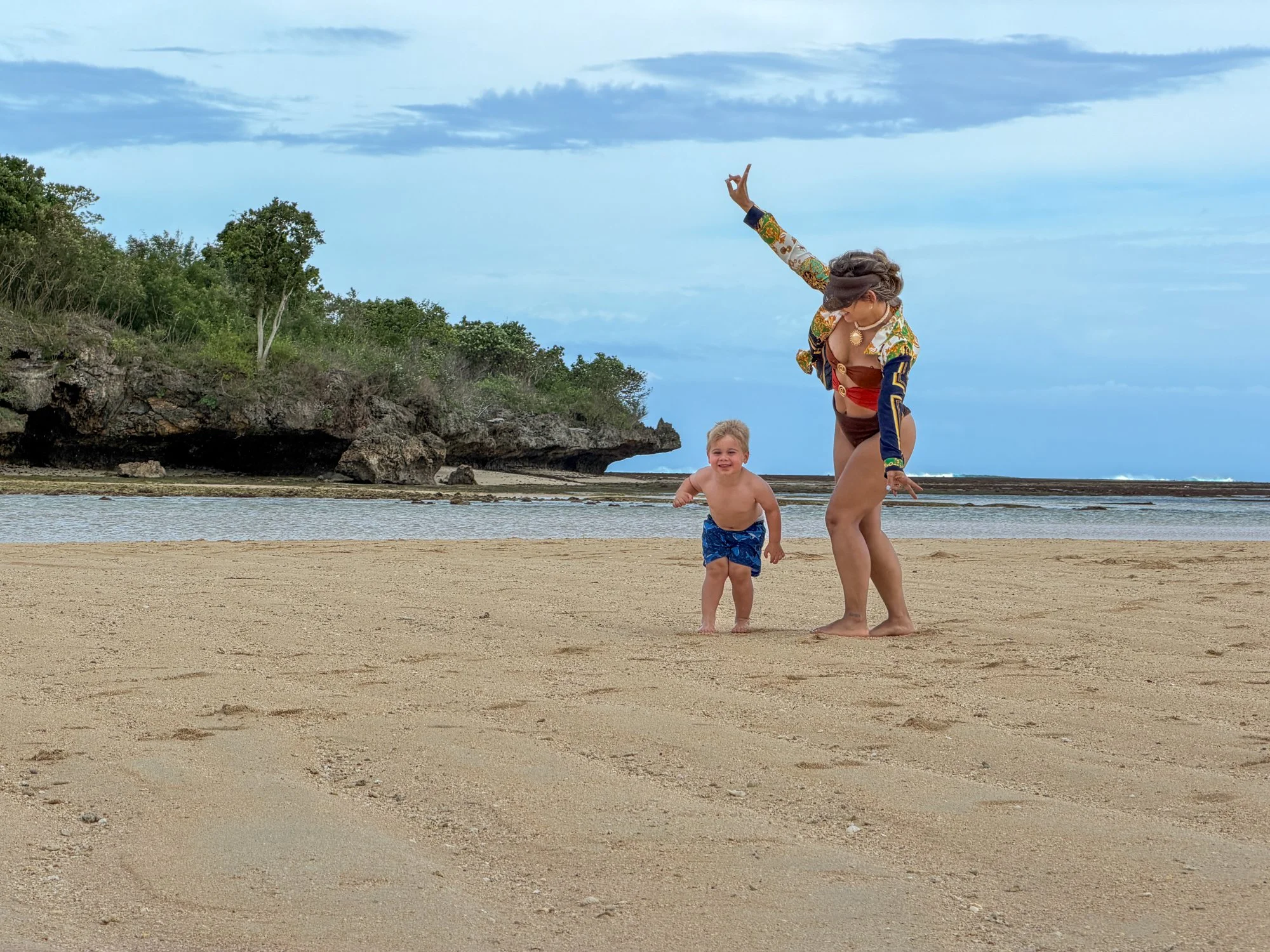 A traveler and young child play together on a quiet beach framed by coastal limestone in Fiji.