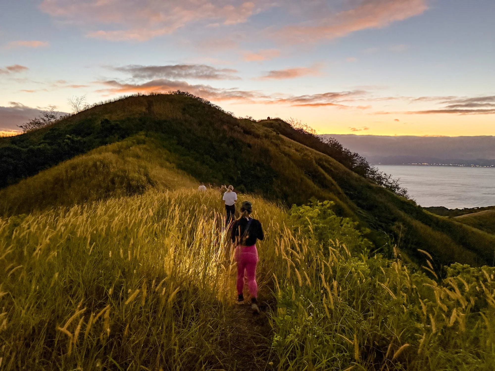Travelers hike through golden grass along a Fijian hillside at sunset.