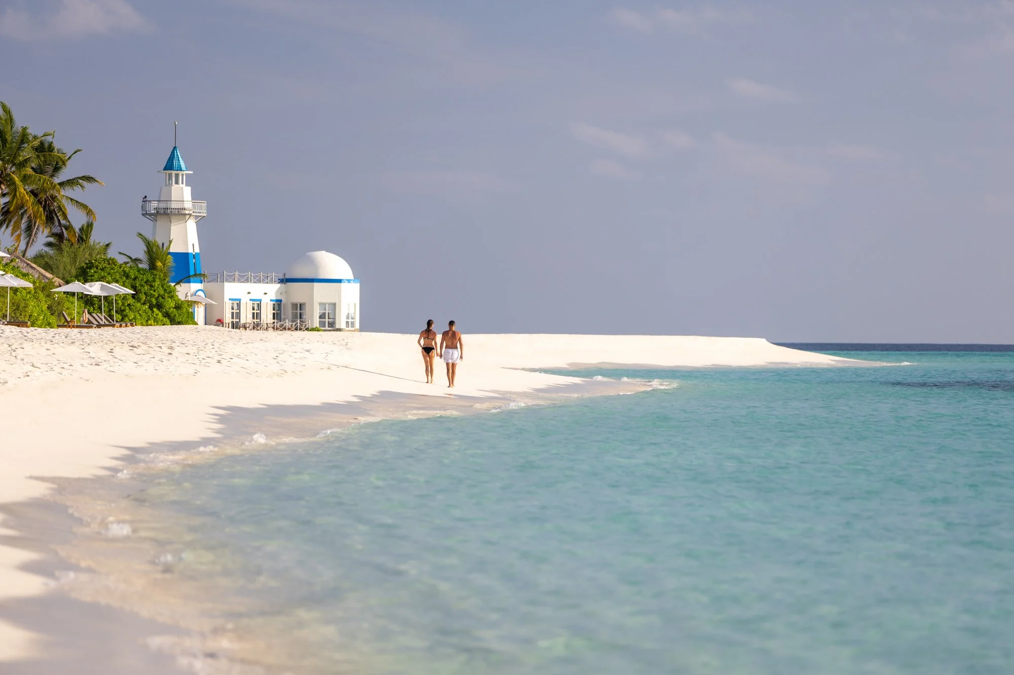 Quiet white-sand beach and blue-and-white lighthouse on a Maldives island.