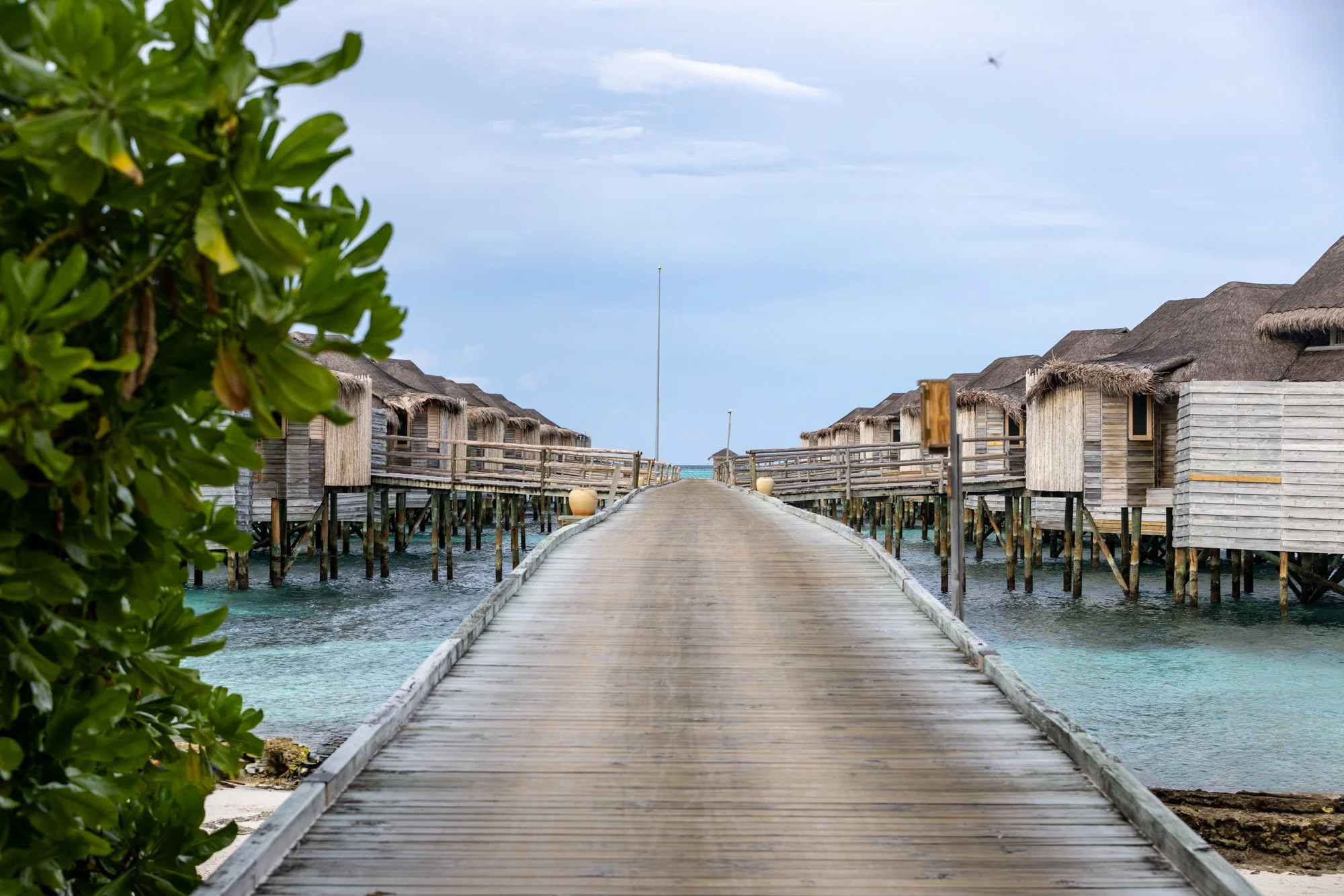 Wooden boardwalk leading between overwater villas above a Maldives lagoon.