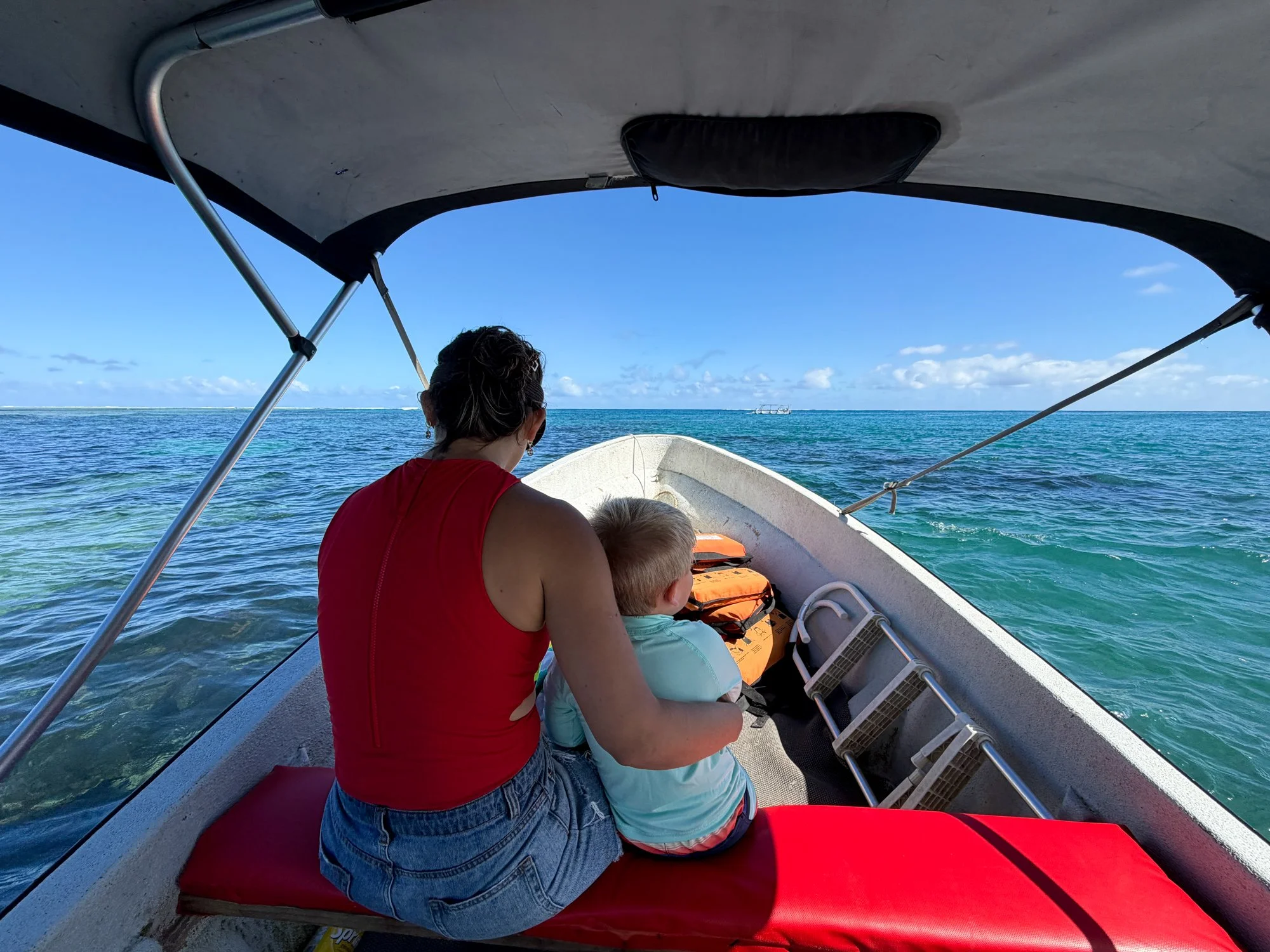 A traveler and young child sit together in a small boat crossing Fiji’s clear blue water.