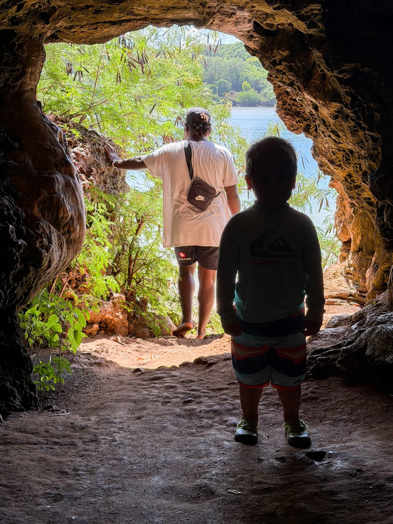 A guide and young child explore the sunlit entrance of a coastal cave in Fiji.
