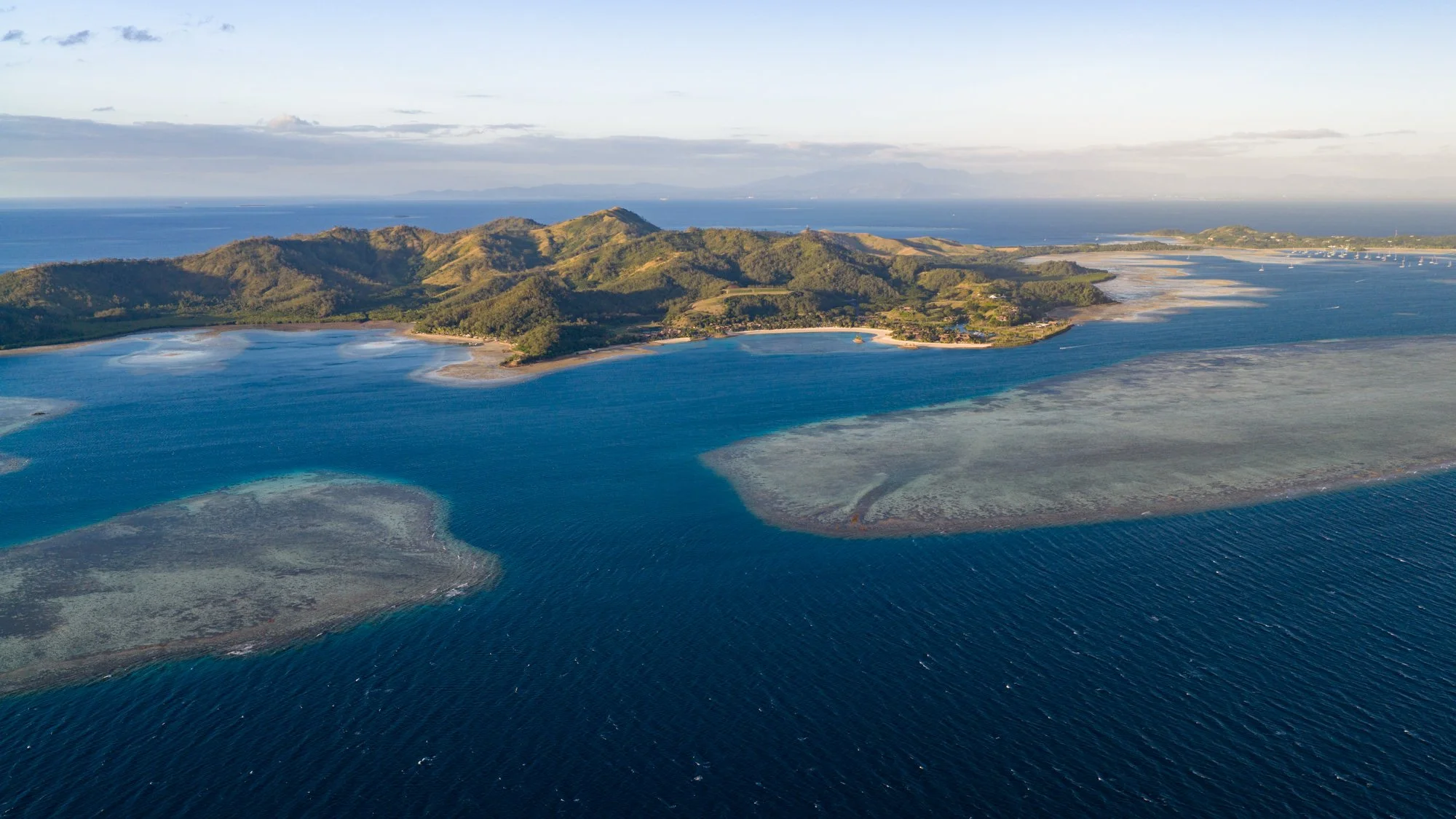 Golden-hour aerial view of green Fijian islands and coral reefs in the South Pacific.