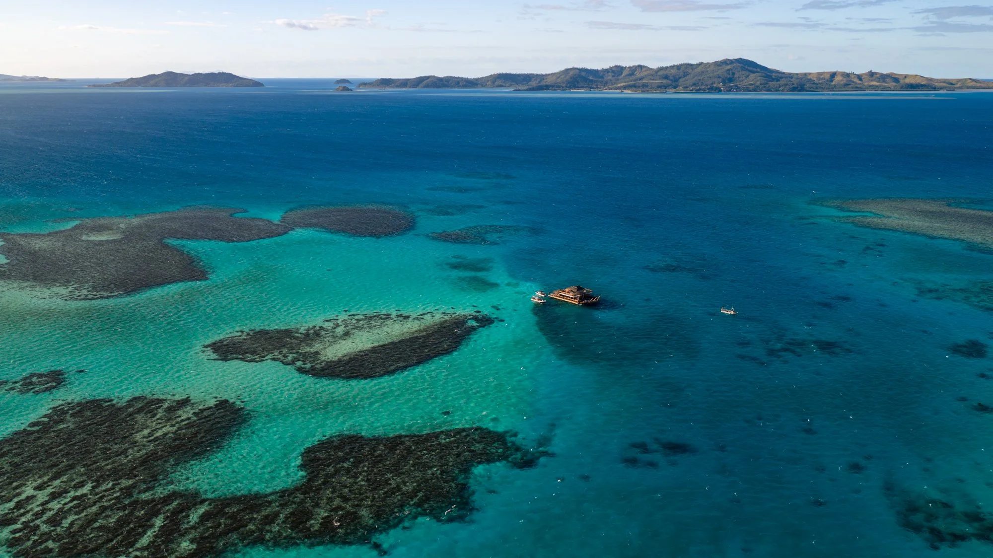 A floating restaurant rests among coral reefs in Fiji’s vivid turquoise and blue water.