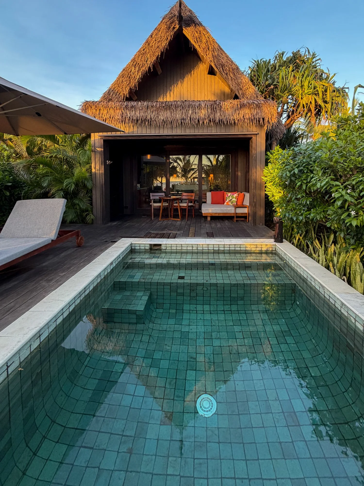 A private plunge pool faces a thatched-roof tropical villa surrounded by lush greenery in Fiji.