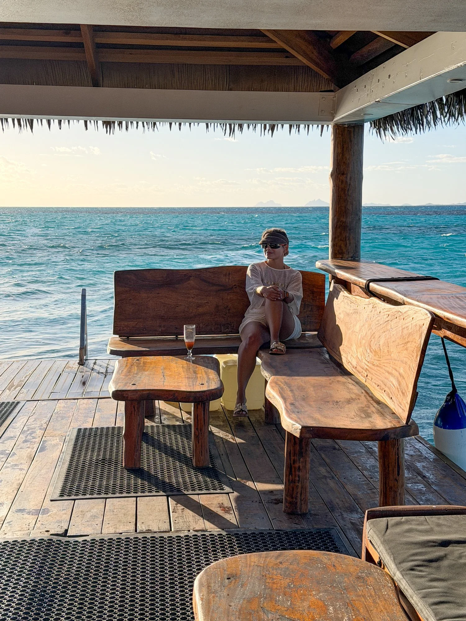 A traveler relaxes on a wooden deck above turquoise water at a floating Fiji restaurant.