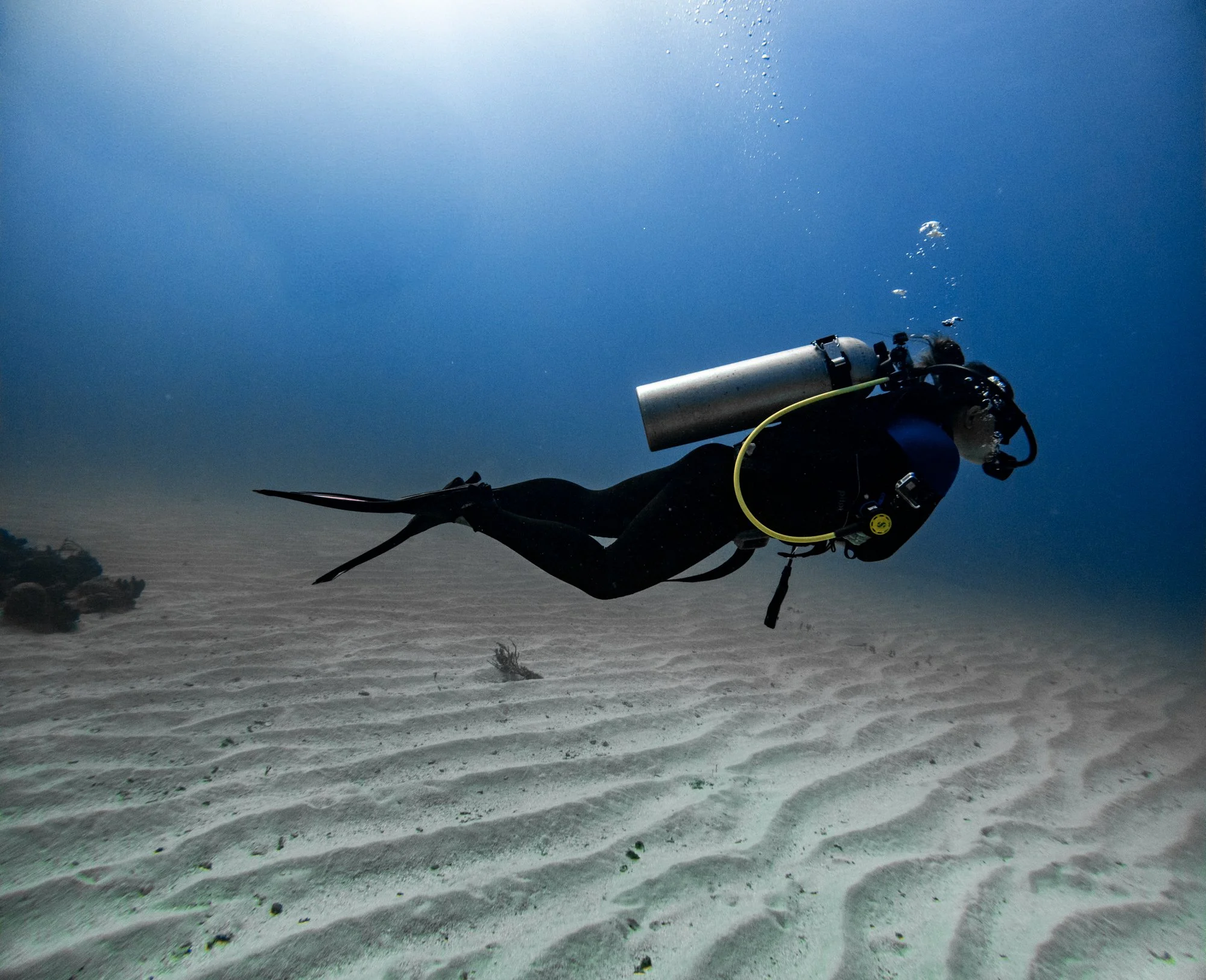 Scuba diver gliding through sunbeams above a sandy reef in Jamaica.