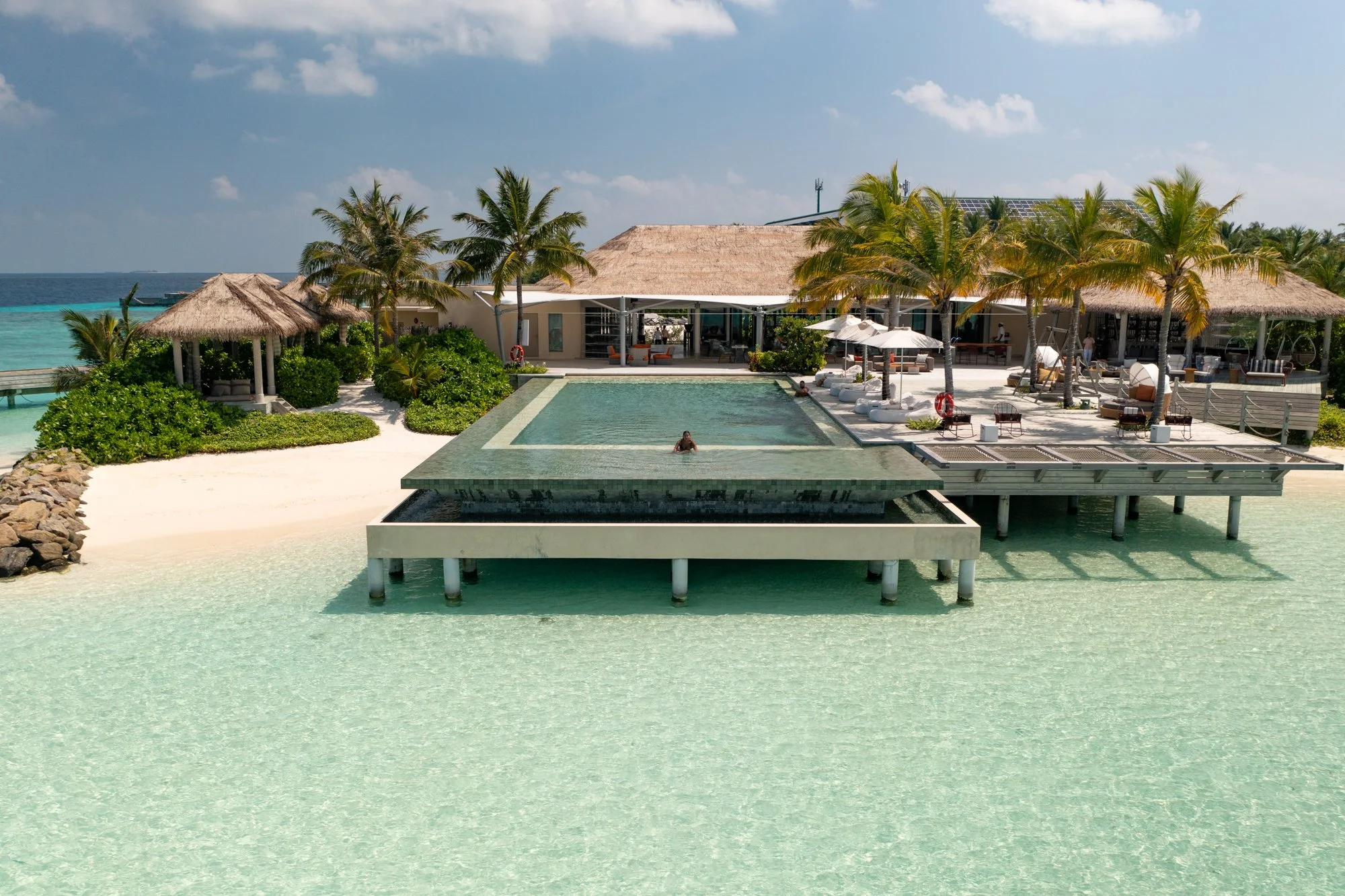 Infinity pool extending over a shallow turquoise lagoon at a Maldives island resort.