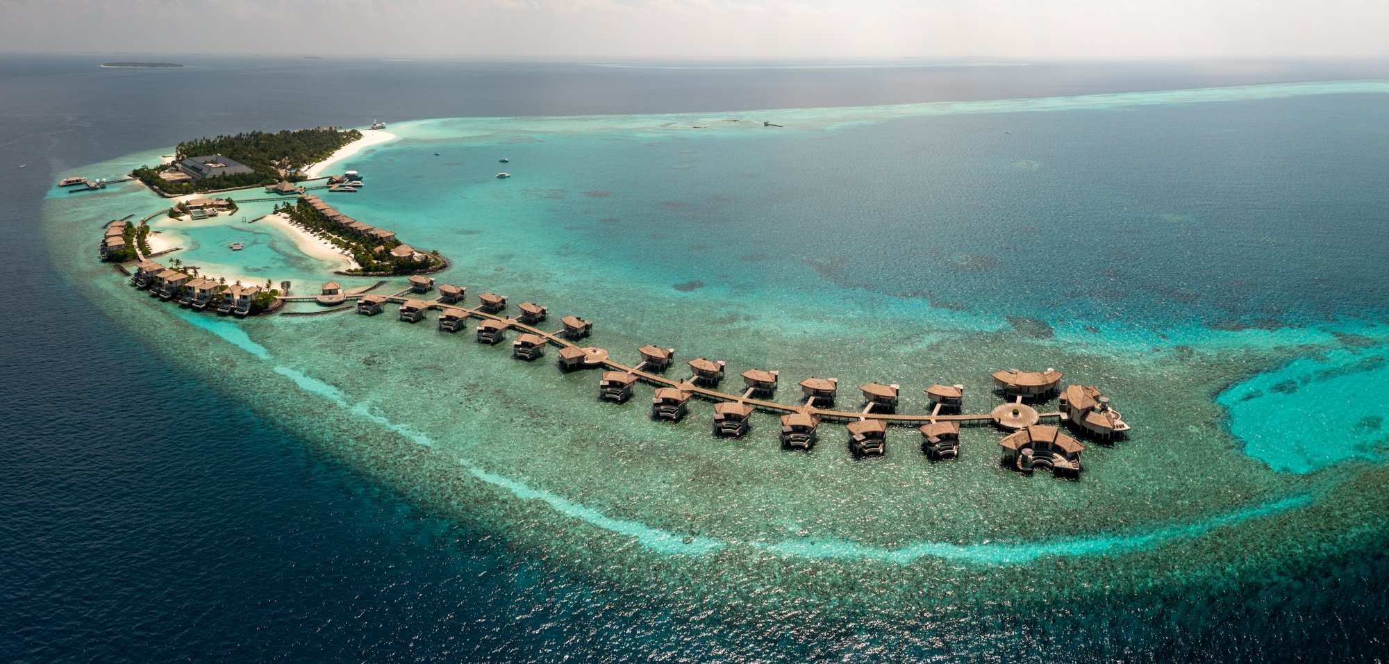 Panoramic aerial view of overwater villas curving across a Maldives coral lagoon.