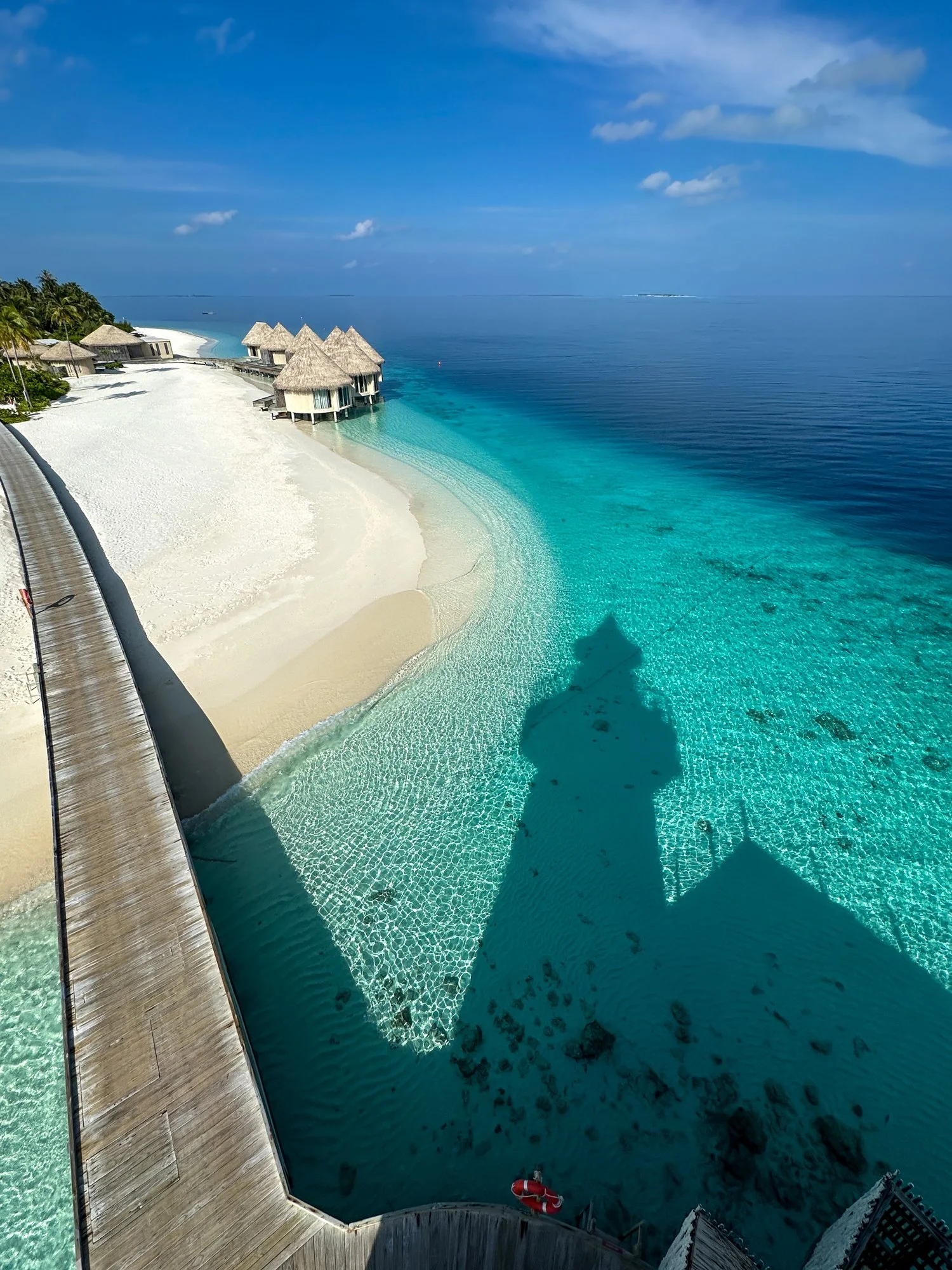 Turquoise Maldives lagoon and white-sand beach viewed from a wooden boardwalk.