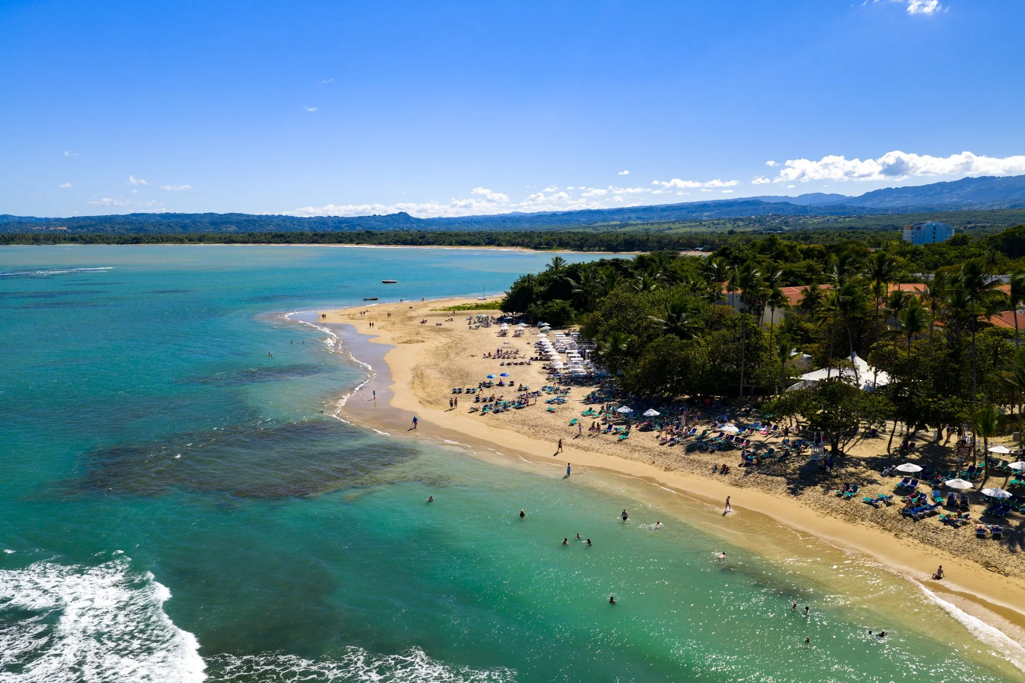 Aerial view of a curving beach and turquoise bay backed by green hills in Puerto Plata.