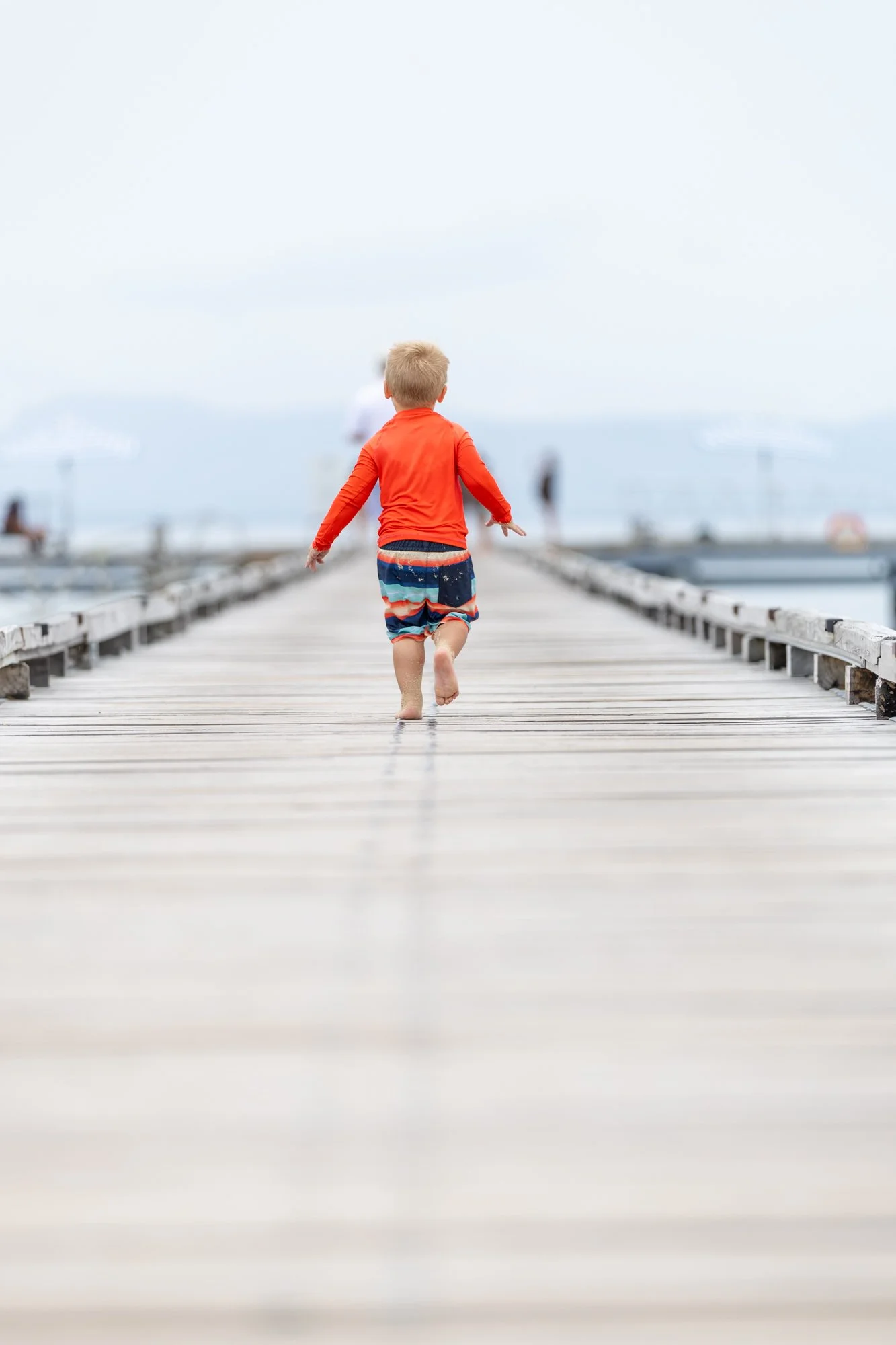 A young child runs barefoot along a wooden pier toward the sea in Fiji.